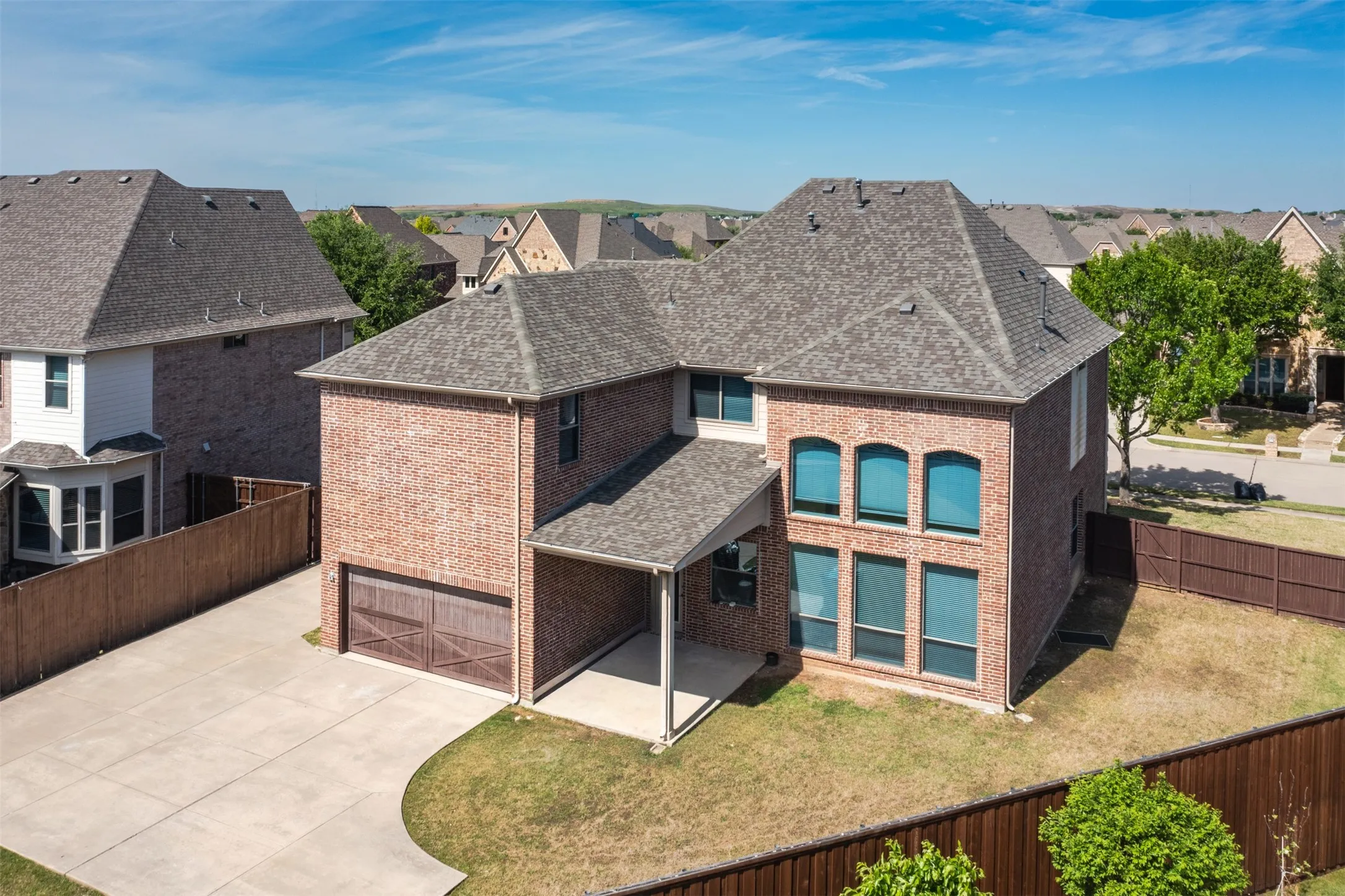 Rear view of house featuring roof with shingles, brick siding, a fenced backyard, a patio, and concrete driveway