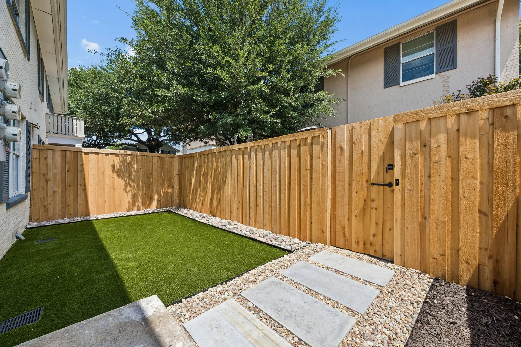 Private outdoor space featuring artificial turf, a wood privacy fence, and a gate with black hardware