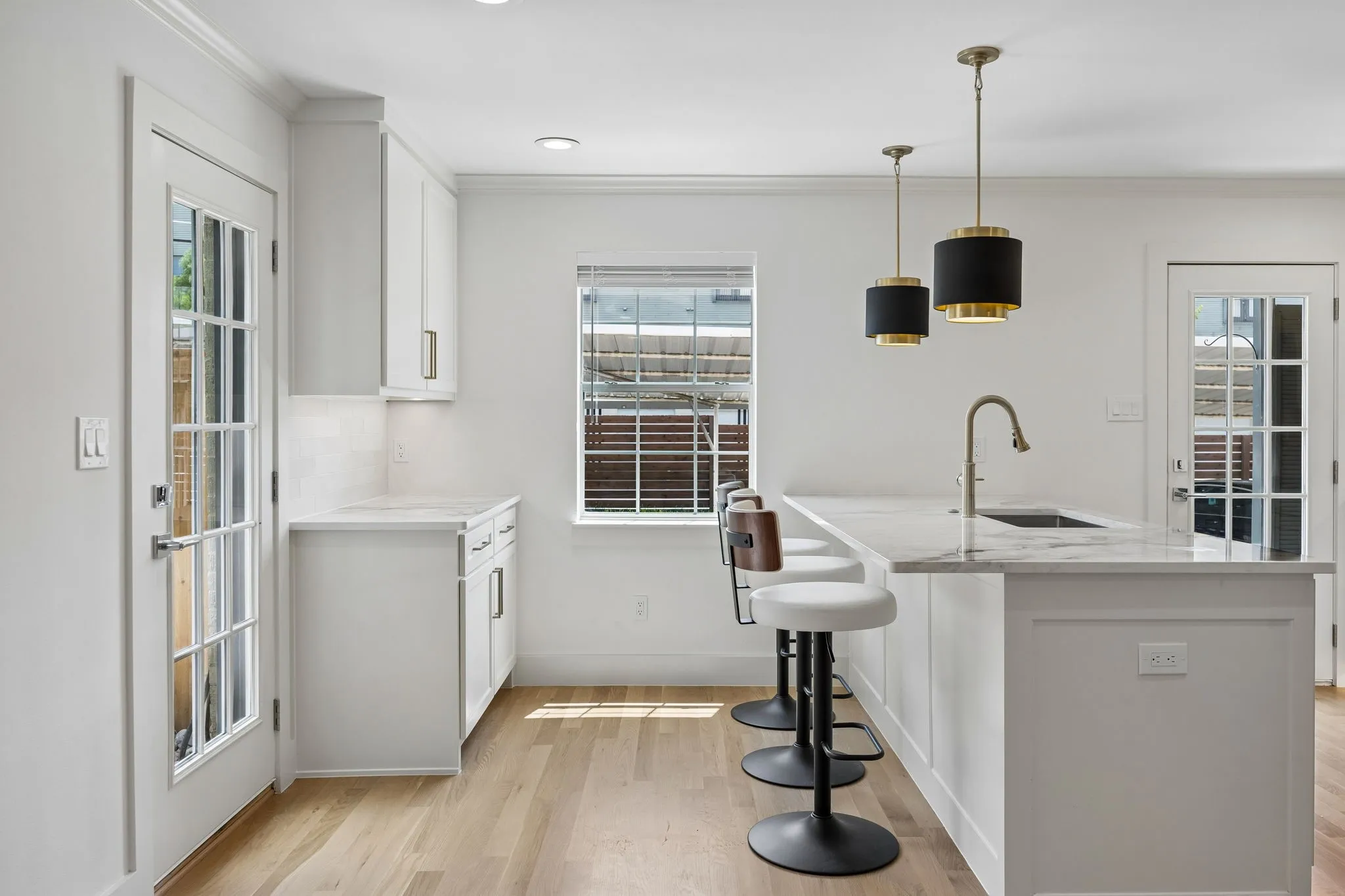 Kitchen featuring an island with seating, pendant lighting, light wood-finish flooring, white cabinetry, and a full-light glass door