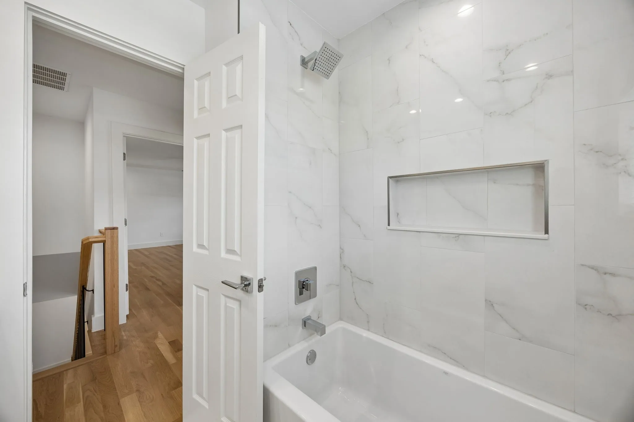 Bathtub with white subway tile surround and recessed niche, featuring a rain shower head and brushed chrome fixtures