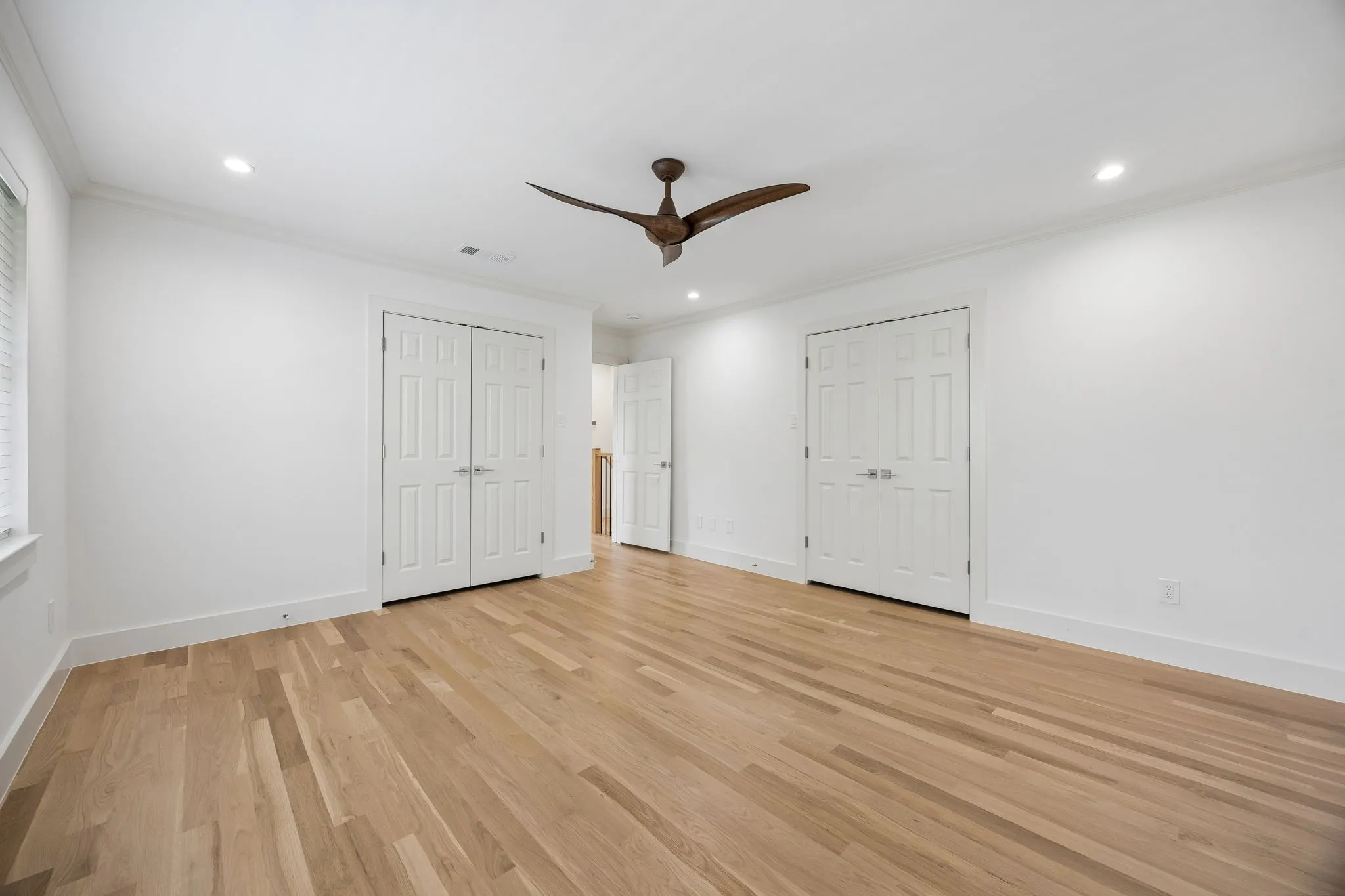 Spacious room featuring wood-finish flooring, recessed lighting, a ceiling fan, and two sets of double-panel doors