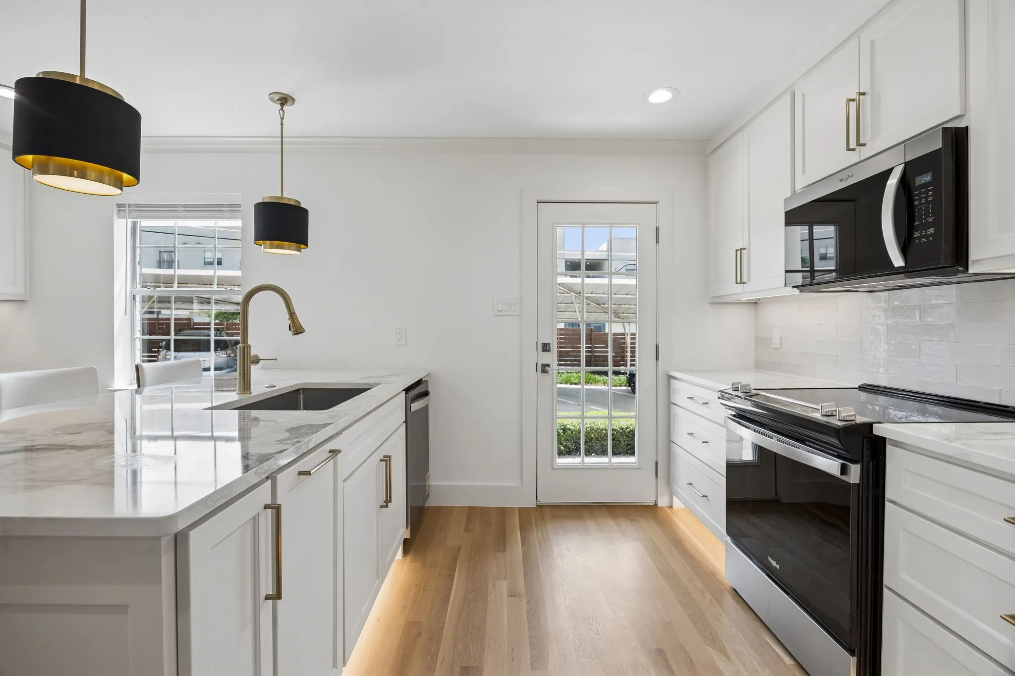Kitchen featuring light wood-finish flooring, white cabinetry with brass hardware, a white subway tile backsplash, and a glass-paneled door