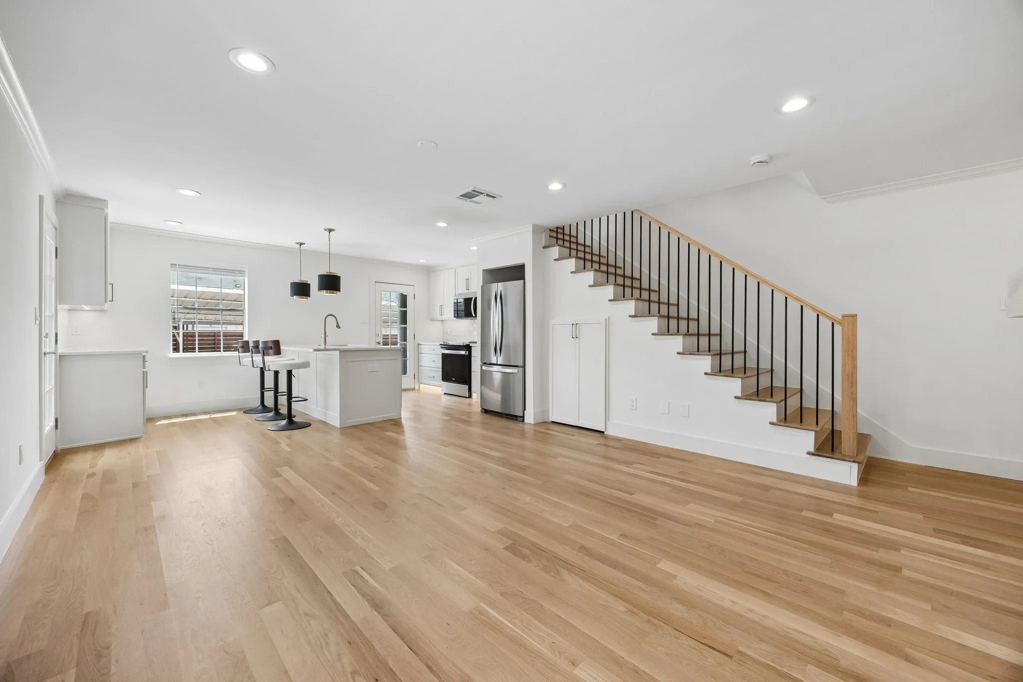 Open-concept living area featuring light wood-finish flooring, recessed lighting, and crown molding