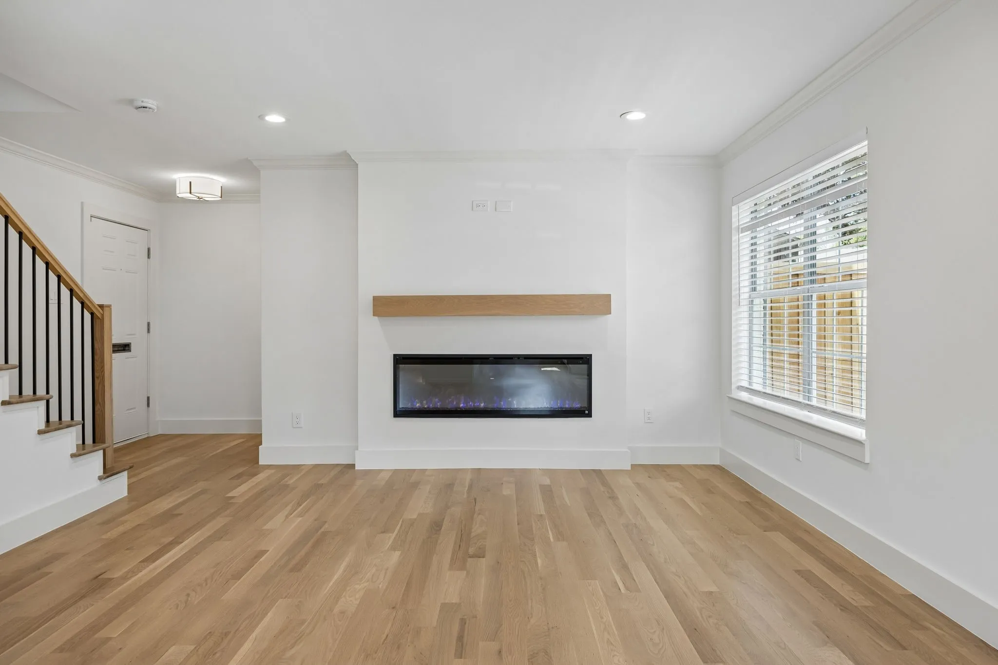 Living area featuring a sleek linear fireplace with a wood mantle, recessed lighting, and wood-finish flooring
