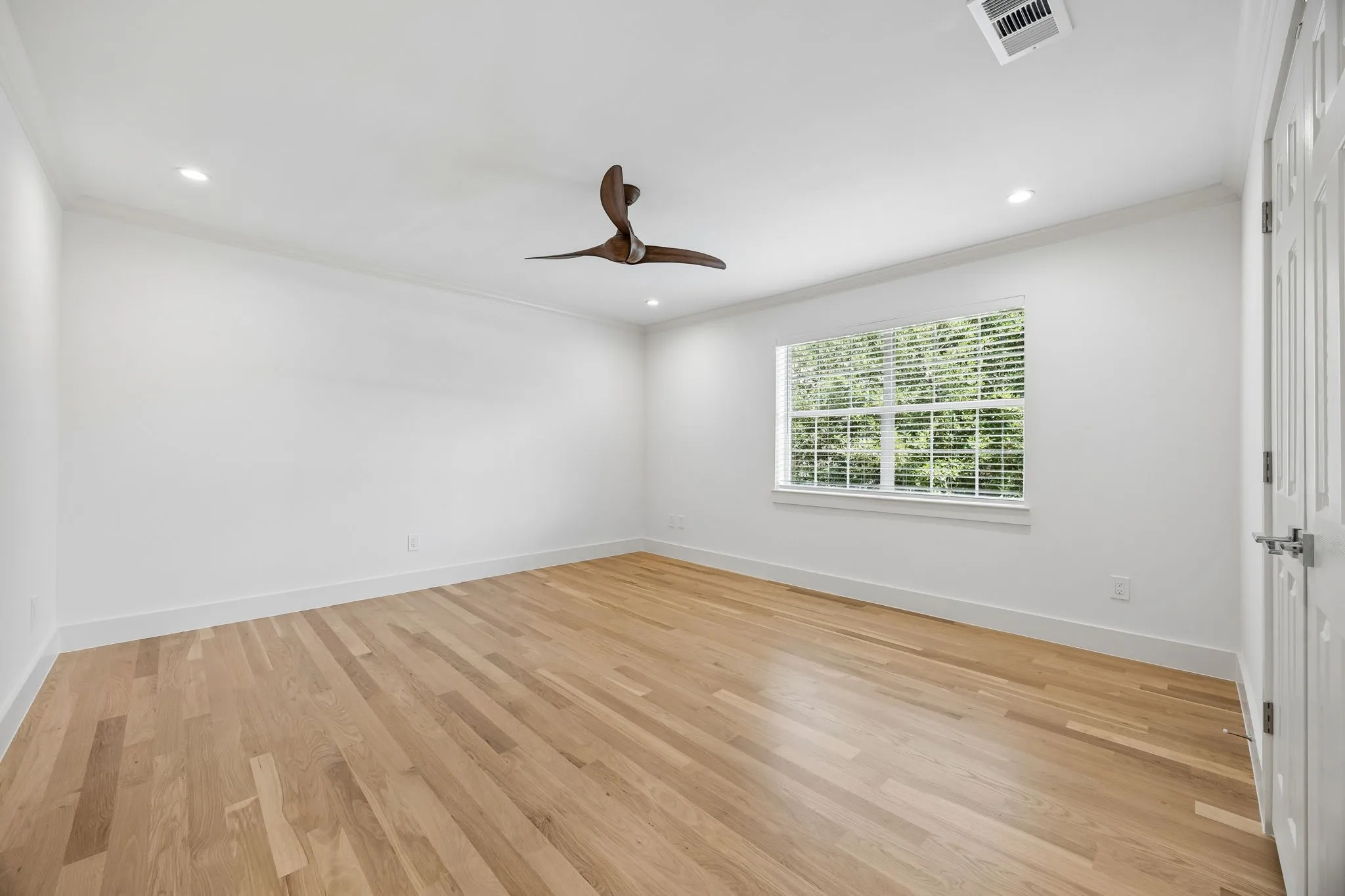 Spacious room featuring wood-finish flooring, white walls, and crown molding