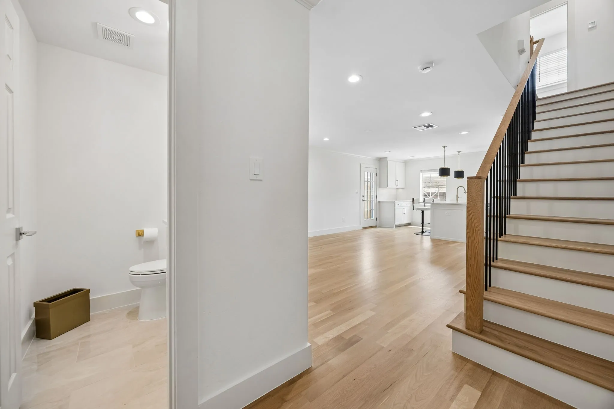 Open concept living space featuring wood-finish flooring, a contemporary staircase with black metal balusters, and a kitchen with an island and pendant lighting