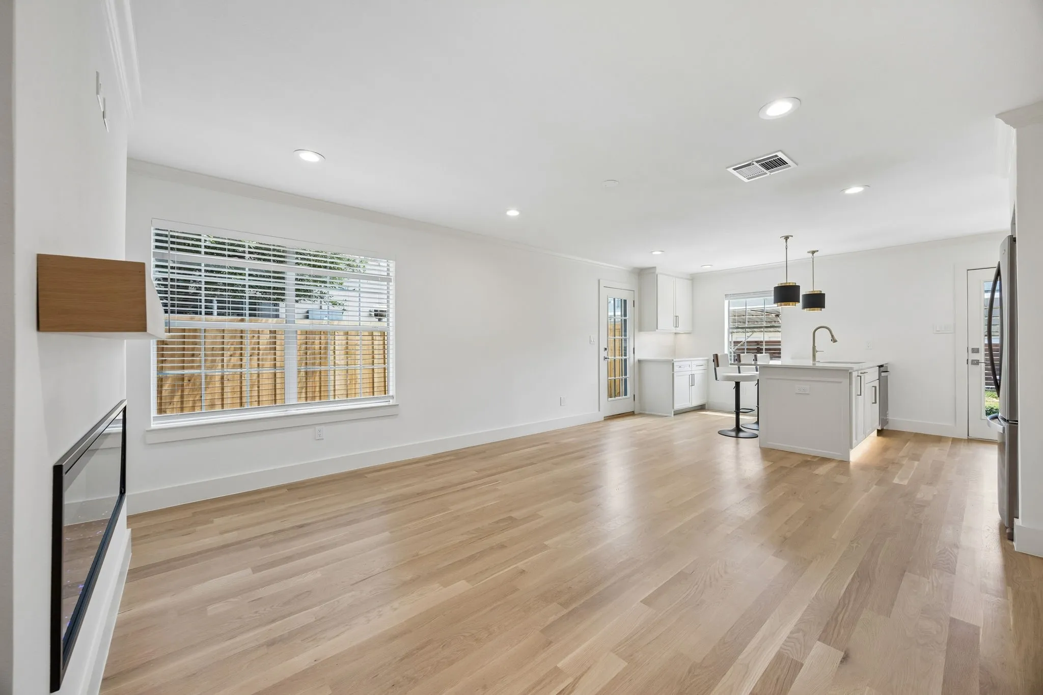 Open-concept living space featuring wood-finish flooring, recessed lighting, and a modern linear fireplace with a wood mantel