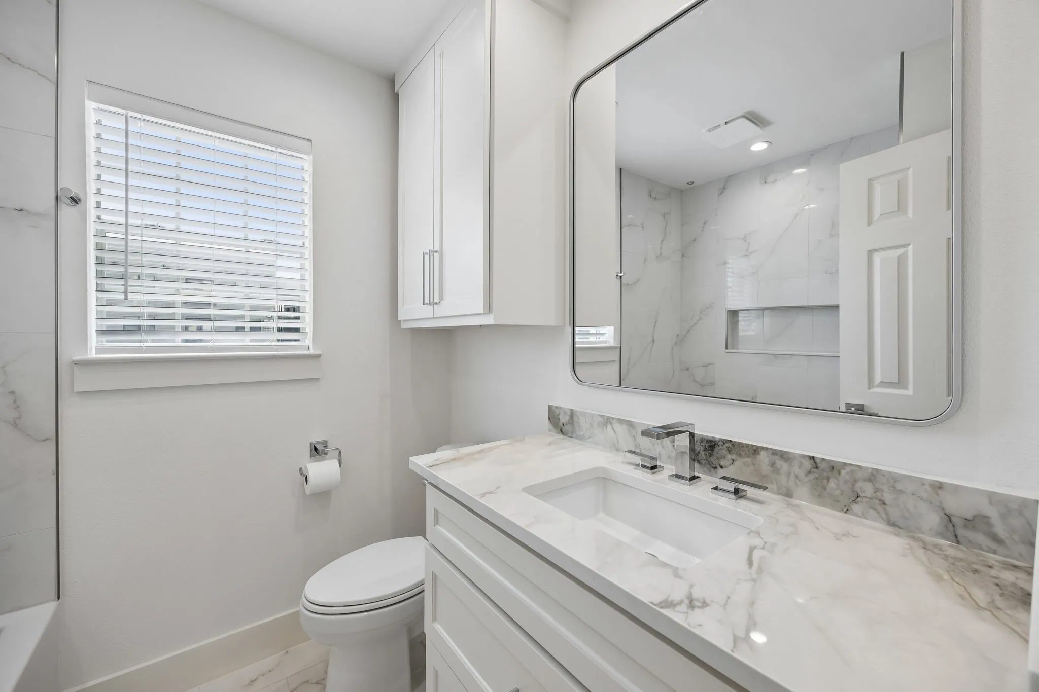Bathroom featuring a single vanity with a white countertop and integrated sink, chrome faucet, and white shaker-style cabinetry