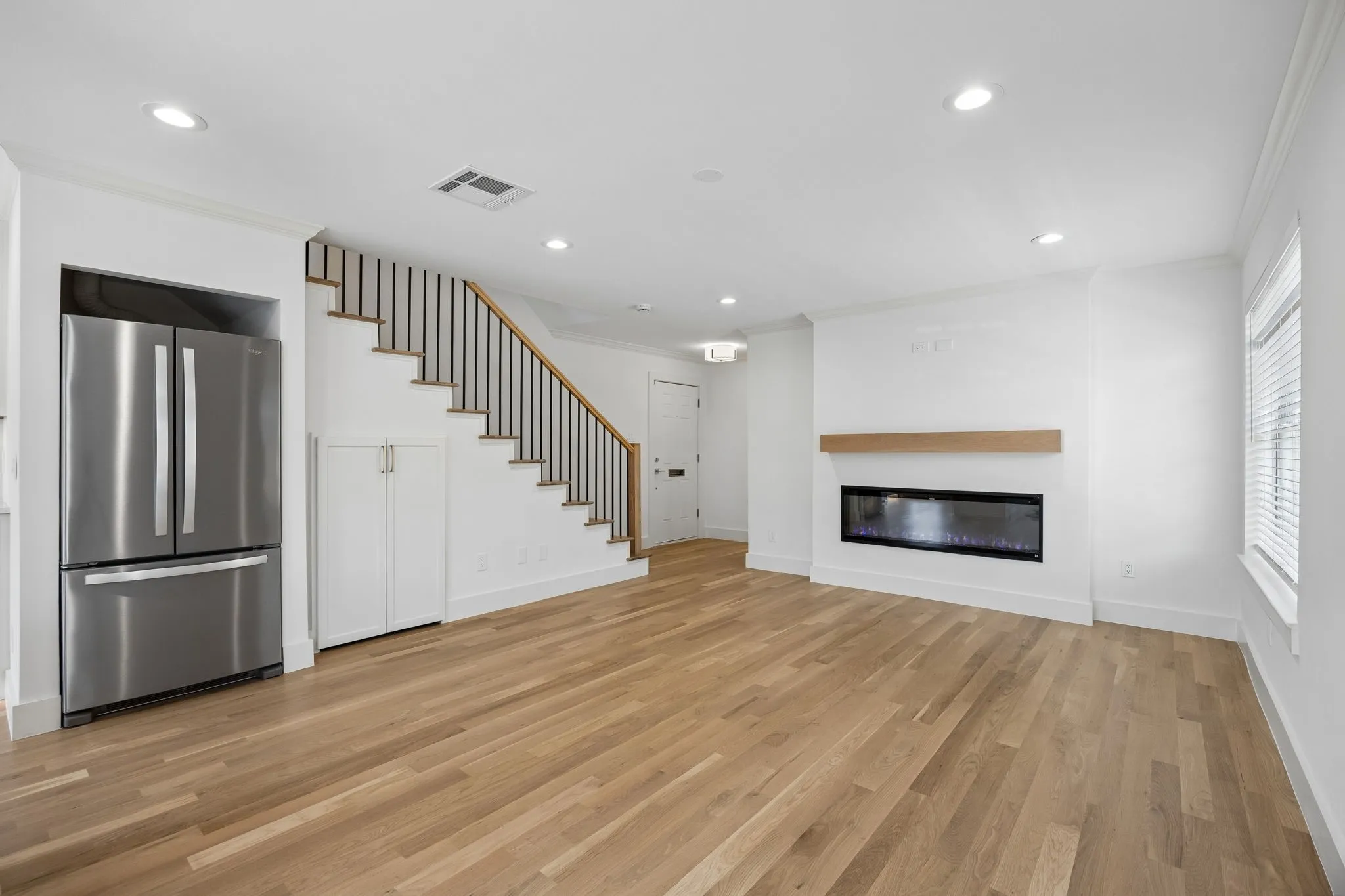 Open-concept living space featuring wood-finish flooring, a linear electric fireplace with a wood mantle, and recessed lighting