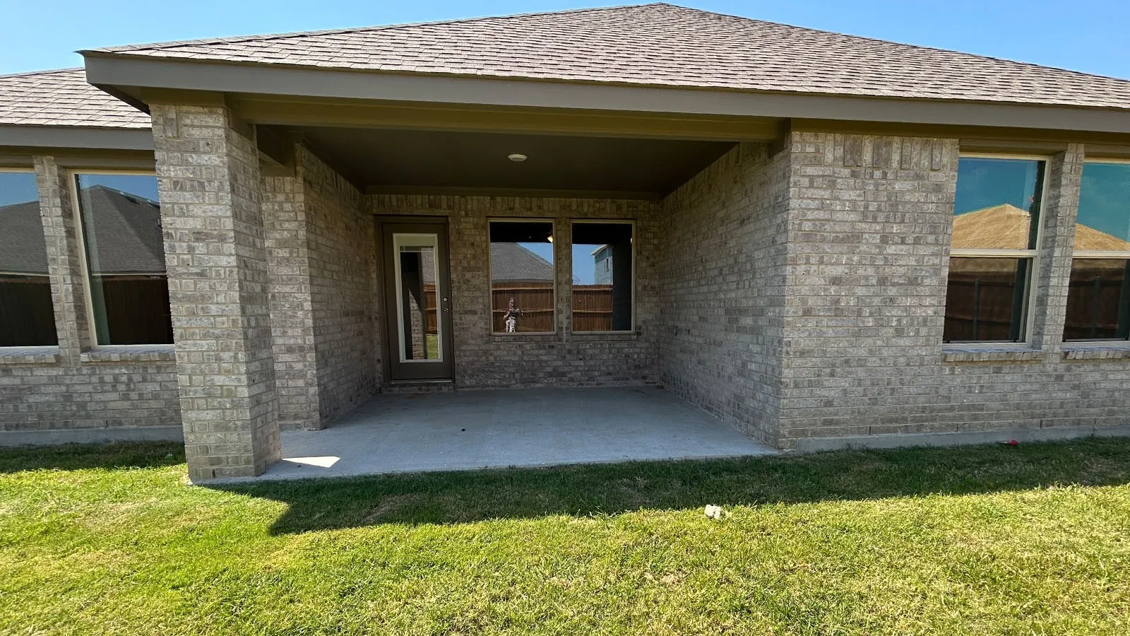 Covered concrete patio with brick support columns, multiple windows, and a glass-paneled exterior door