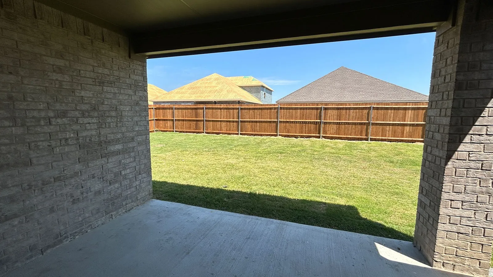 Covered patio with brick-clad columns, concrete flooring, and a fully fenced backyard featuring a manicured lawn