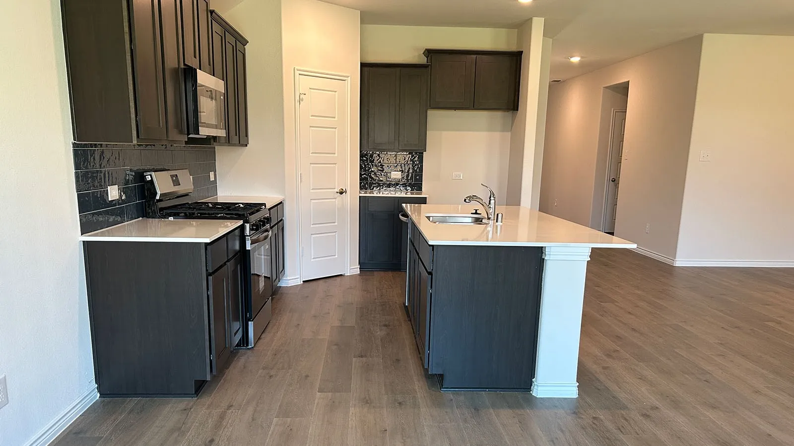 Kitchen featuring dark wood-finish cabinetry, stainless steel appliances, a tile backsplash, and an island with a breakfast bar