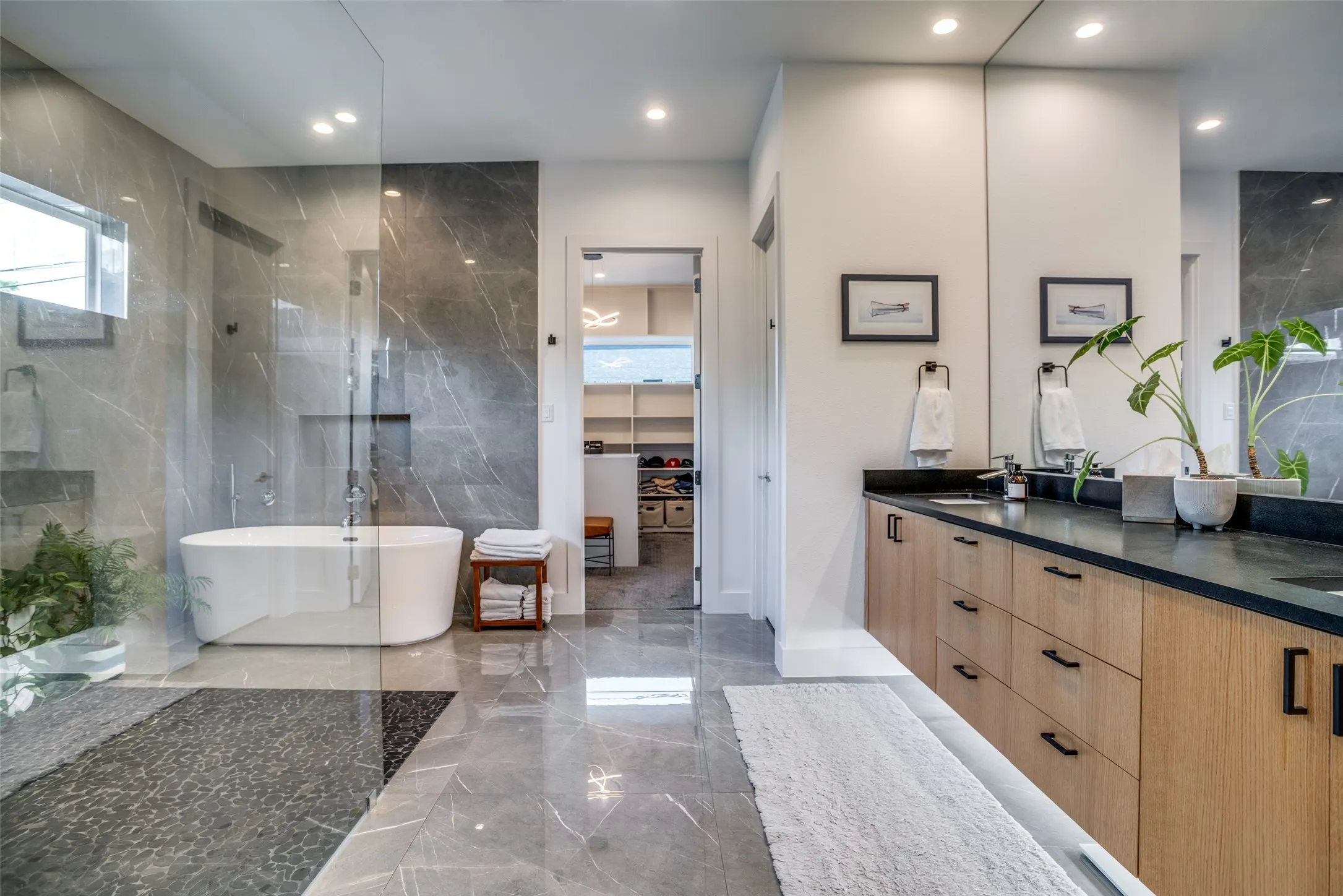Ensuite bathroom with marble tiled floors, a free standing vessel tub, a huge seamless walk in shower with a high window and stone tiled walls.