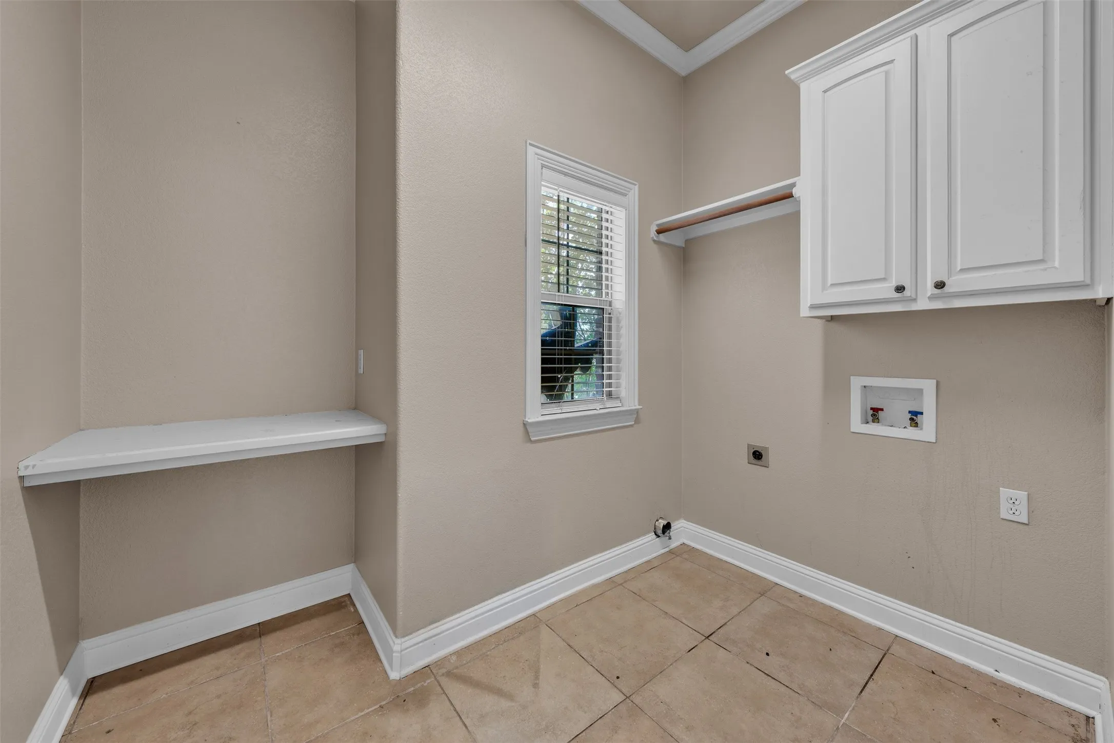 Utility space featuring tiled flooring, a built-in white shelf, and white upper cabinetry