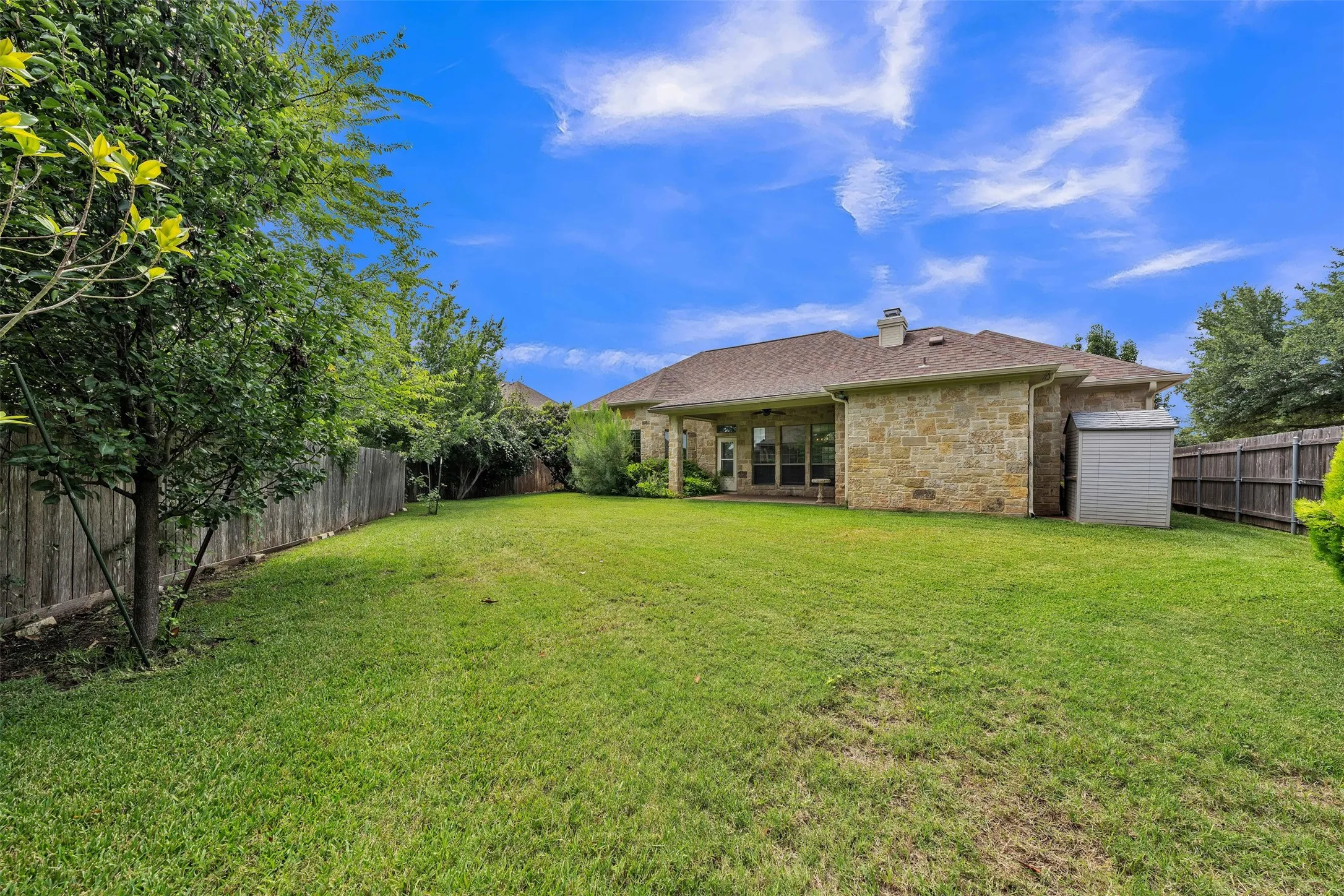 Expansive green lawn with a stone exterior residence, featuring a covered patio and a detached storage shed