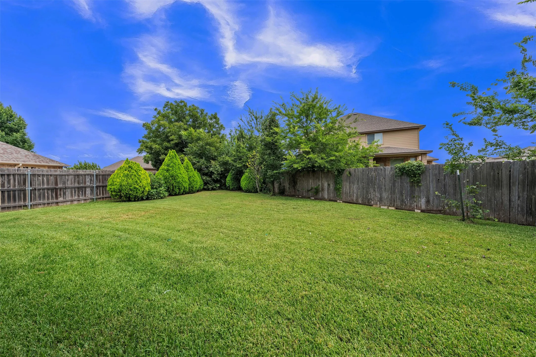 Expansive backyard featuring a large green lawn, mature trees, and a full privacy fence