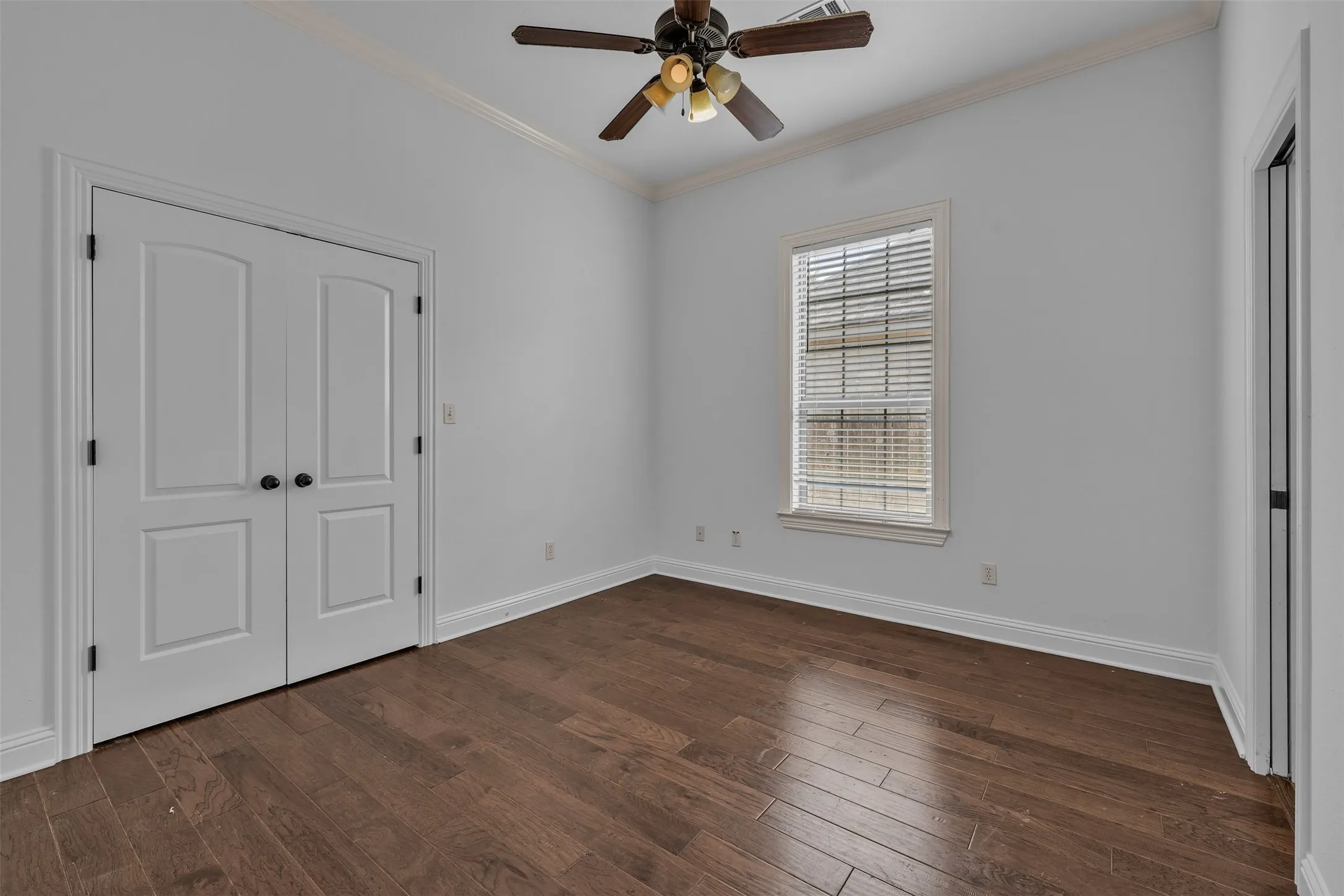 Room featuring wood-finish flooring, a window with blinds, a ceiling fan, and white double doors
