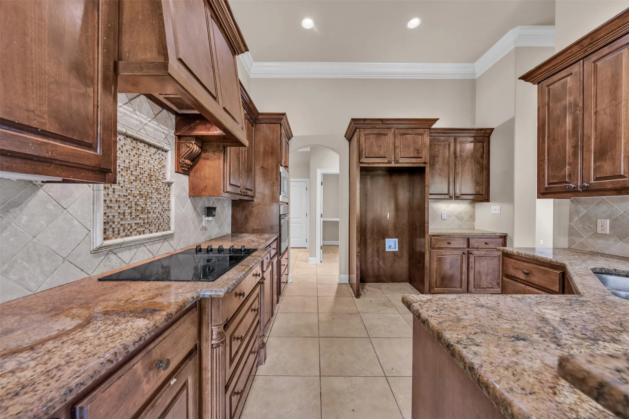 Kitchen featuring extensive wood cabinetry, granite countertops, an integrated cooktop, tile flooring, and a decorative mosaic tile backsplash