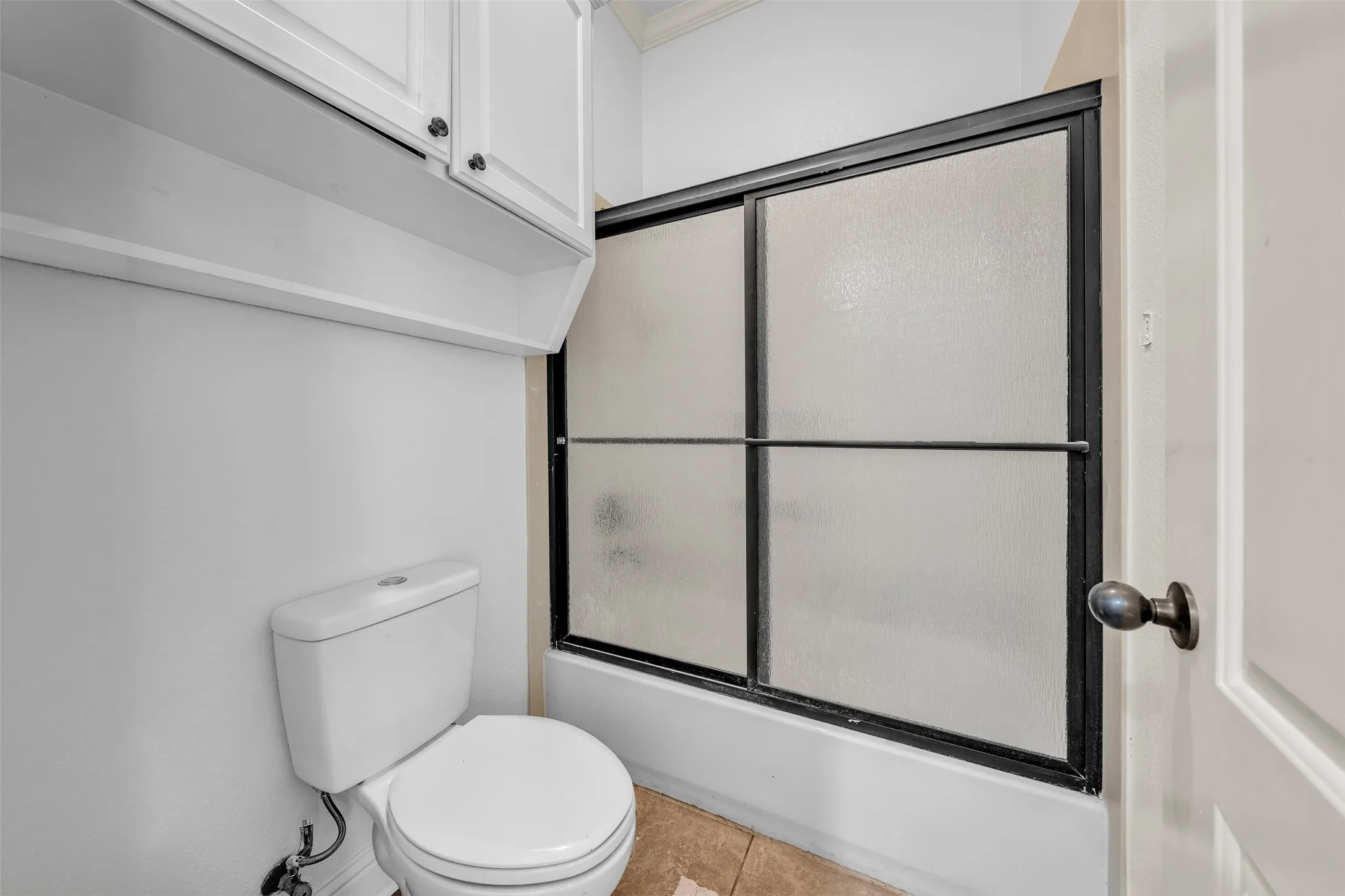 Bathroom featuring a white toilet, enclosed shower with frosted glass, white upper cabinetry, and a shelf