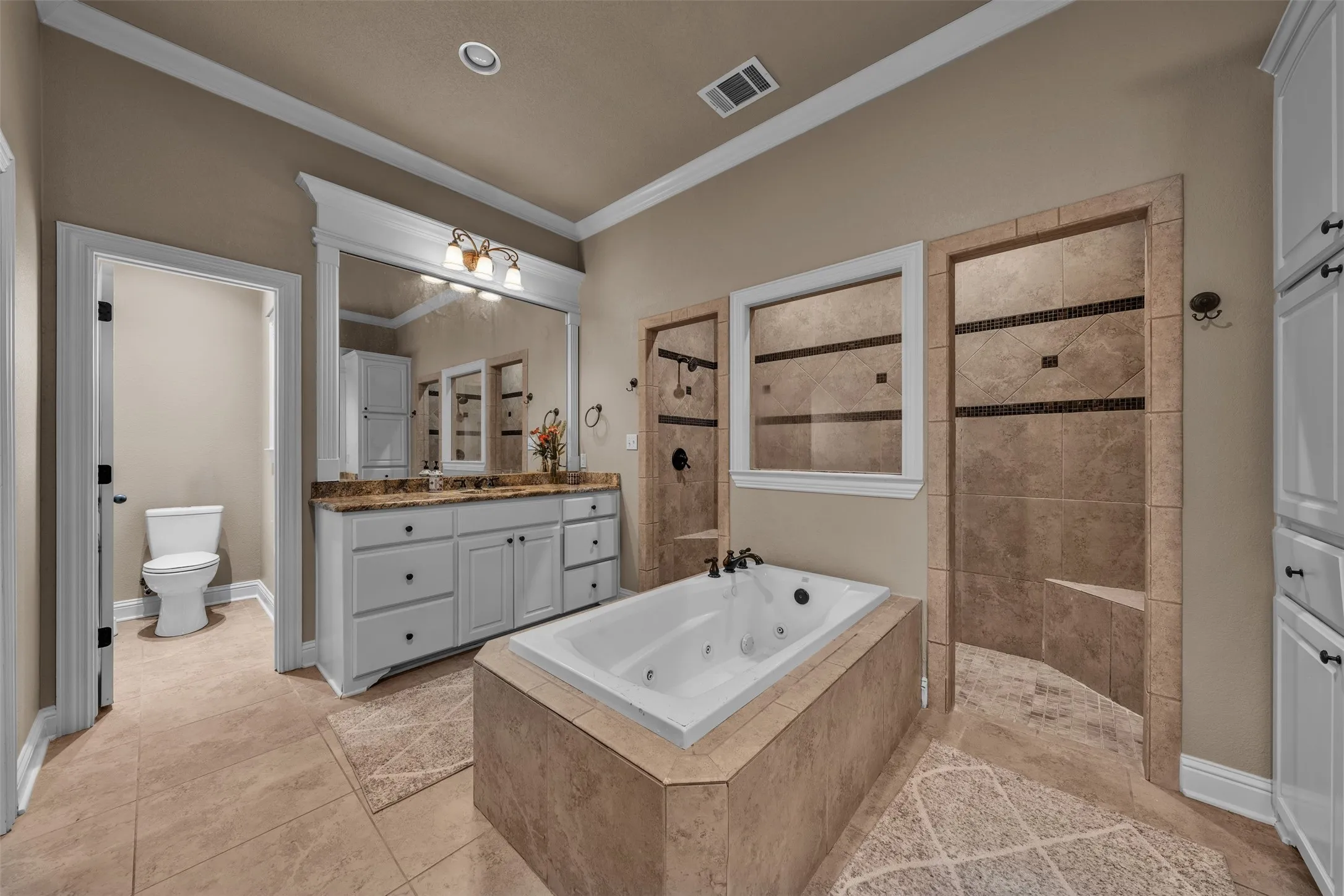 Bathroom featuring a jetted tub, dual walk-in showers with tile surround, a double vanity with granite-style countertop, and ample built-in cabinetry