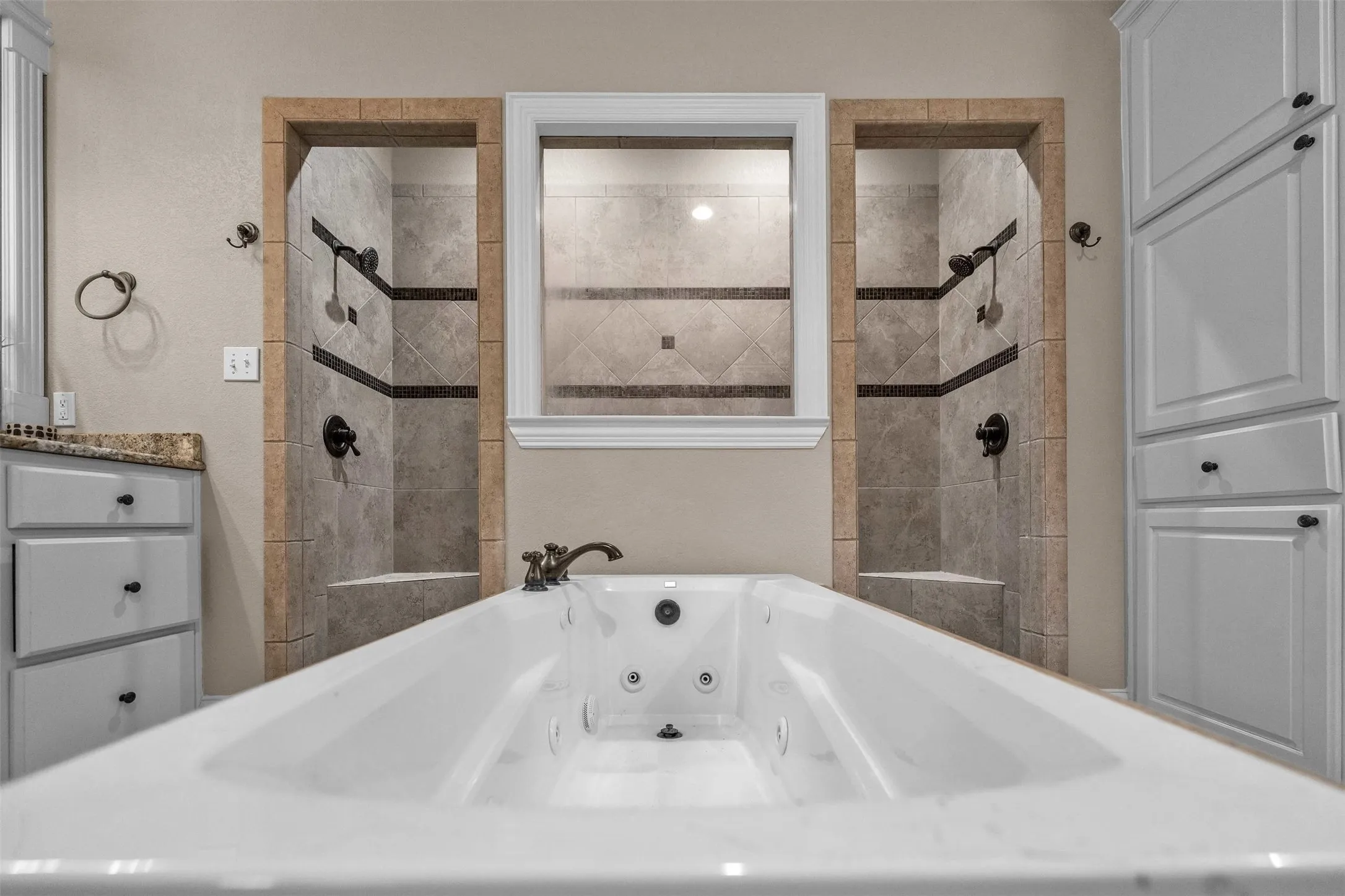 Spacious white soaking tub with bronze-finish fixtures, flanked by two walk-in tiled showers with built-in benches and dark bronze-finish shower heads
