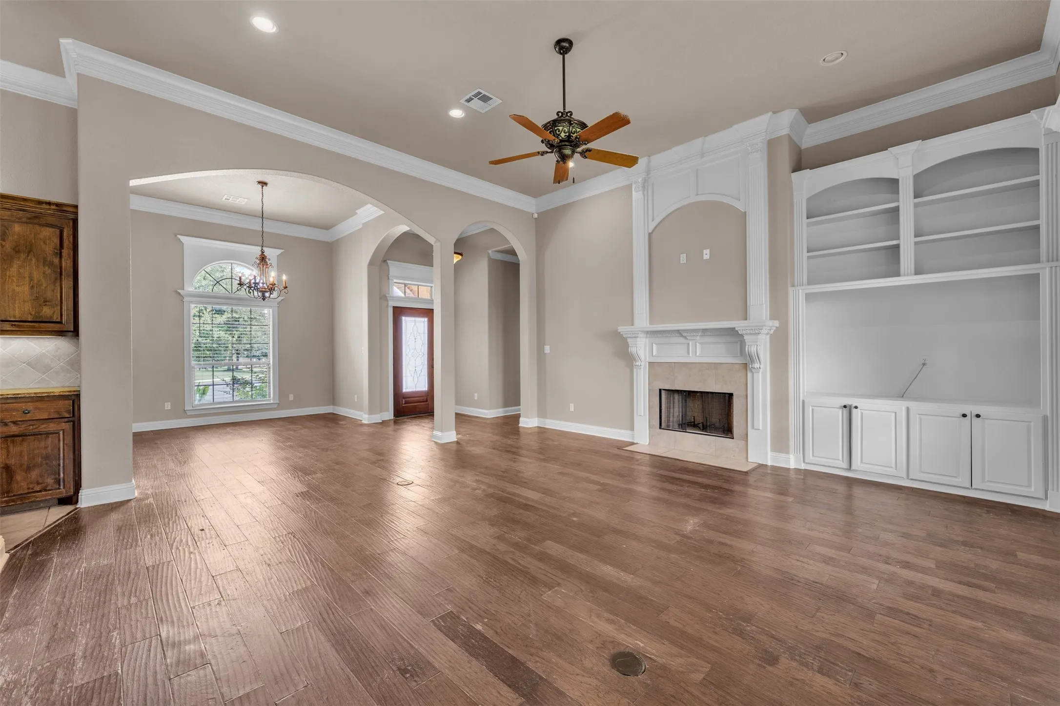 Spacious living area featuring wood-finish flooring, a decorative fireplace with stone surround, and built-in white cabinetry with shelving