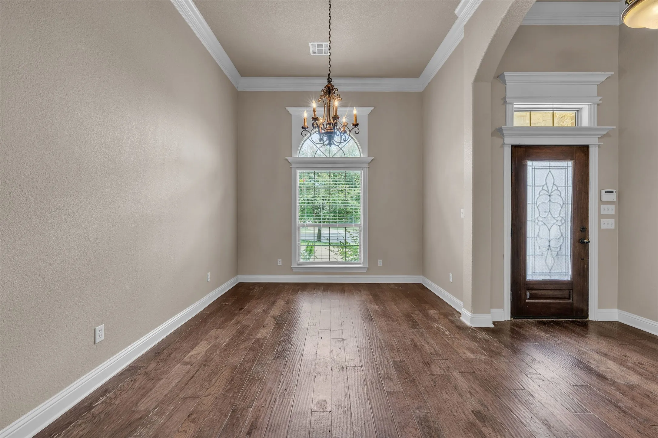 Spacious room featuring wood-finish flooring, neutral wall tones, and extensive crown molding