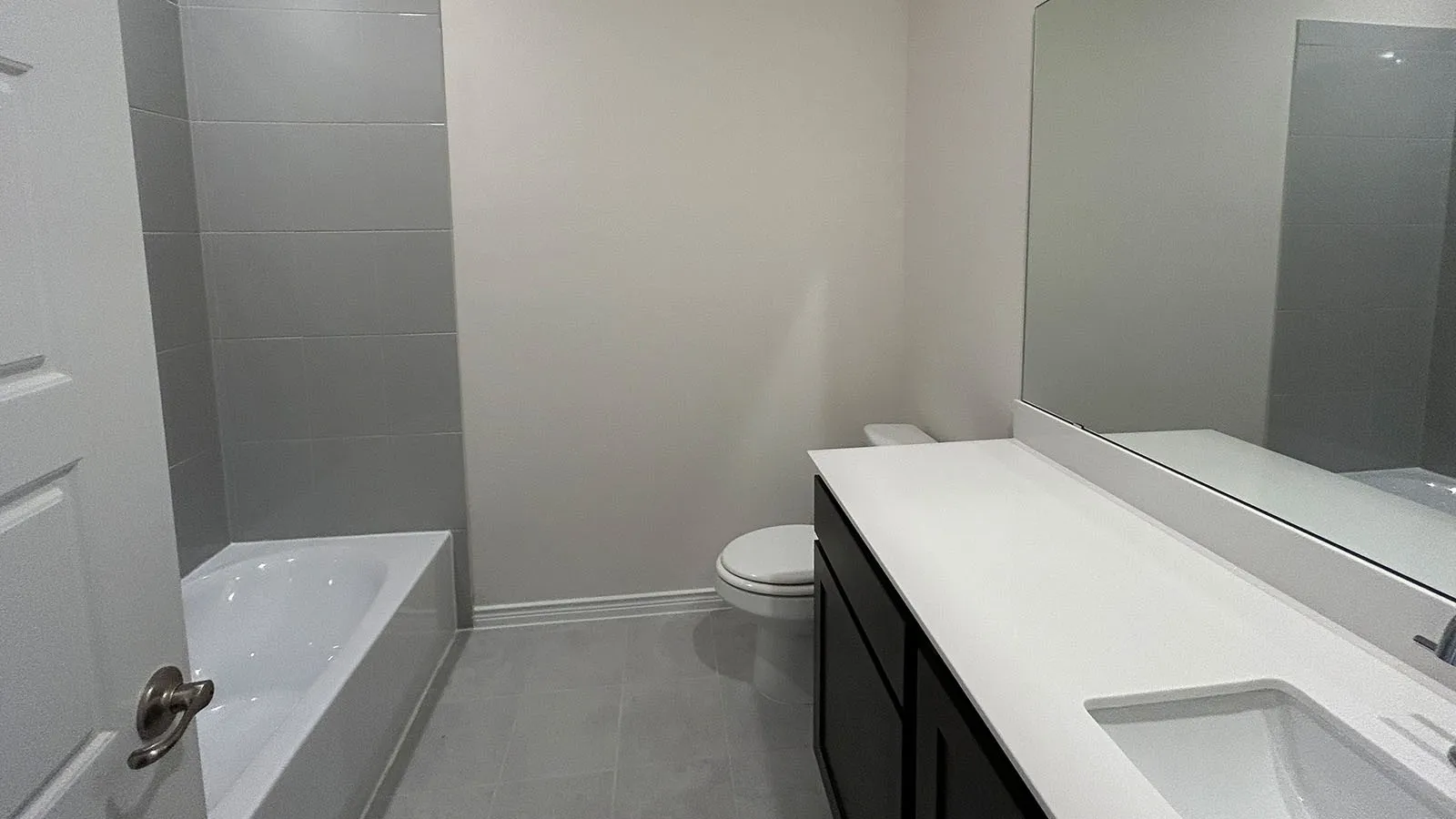 Bathroom with a white bathtub, gray wall tiling, and a dark wood-finish vanity with a white countertop and integrated sink