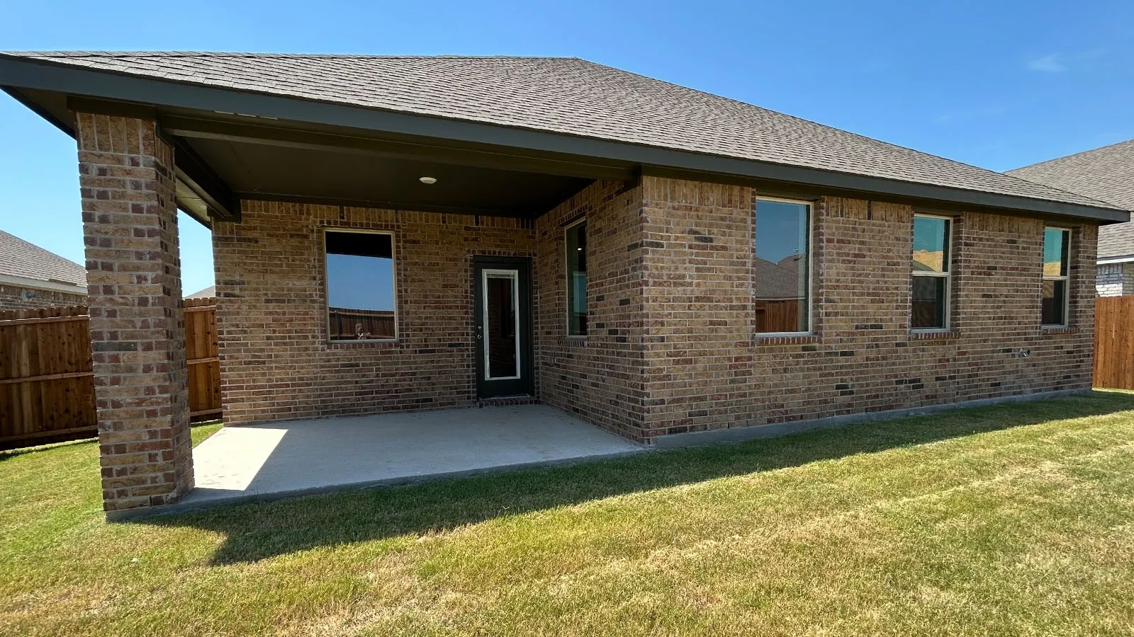 Brick exterior with a covered concrete patio and multiple windows