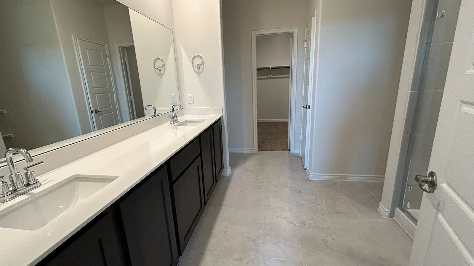 Dual vanity with undermount sinks, expansive mirror, dark wood-finish cabinetry, light-toned countertop, and light-toned tile flooring