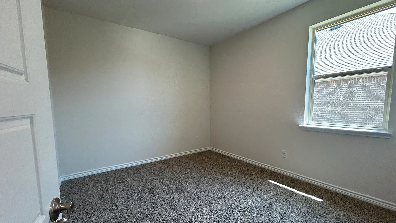 Neutral wall paint, textured carpeting, and a window with a white frame