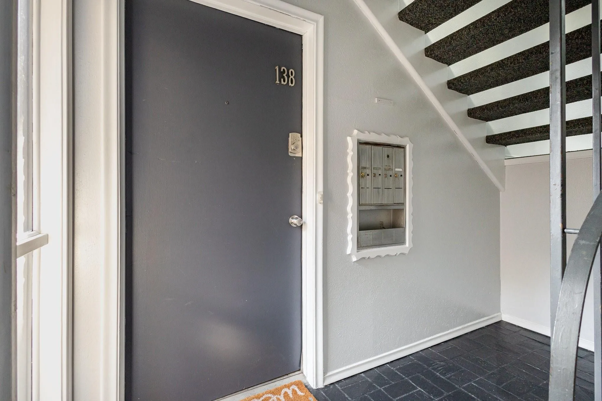 Entryway featuring a dark paneled door with address numbers, a wall-mounted mailbox unit, a black metal staircase with textured treads, and dark tile flooring