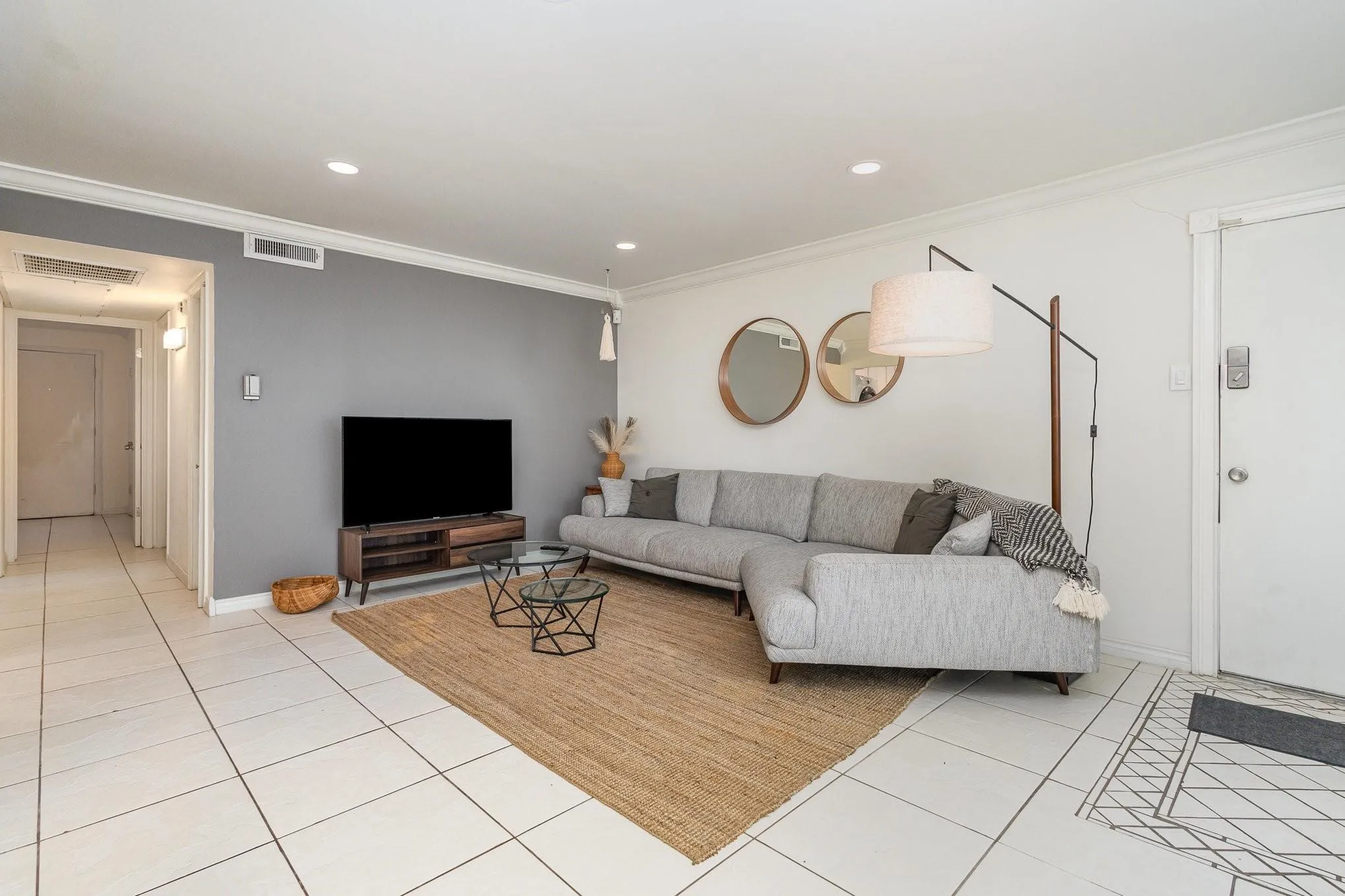 Living area featuring large format floor tiles, a contrasting accent wall, and crown molding