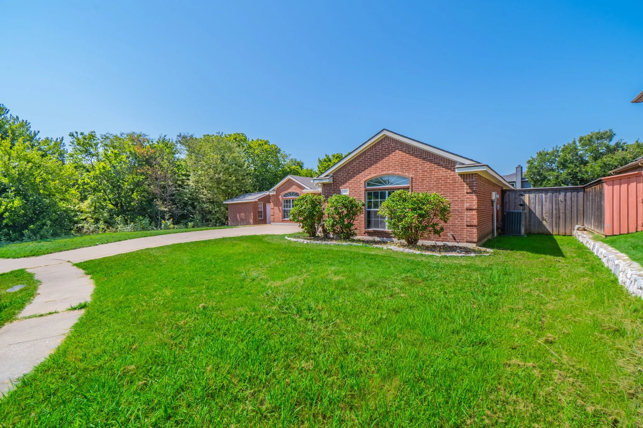 Brick exterior featuring an arched window, a concrete driveway, a wood fence, and mature landscaping