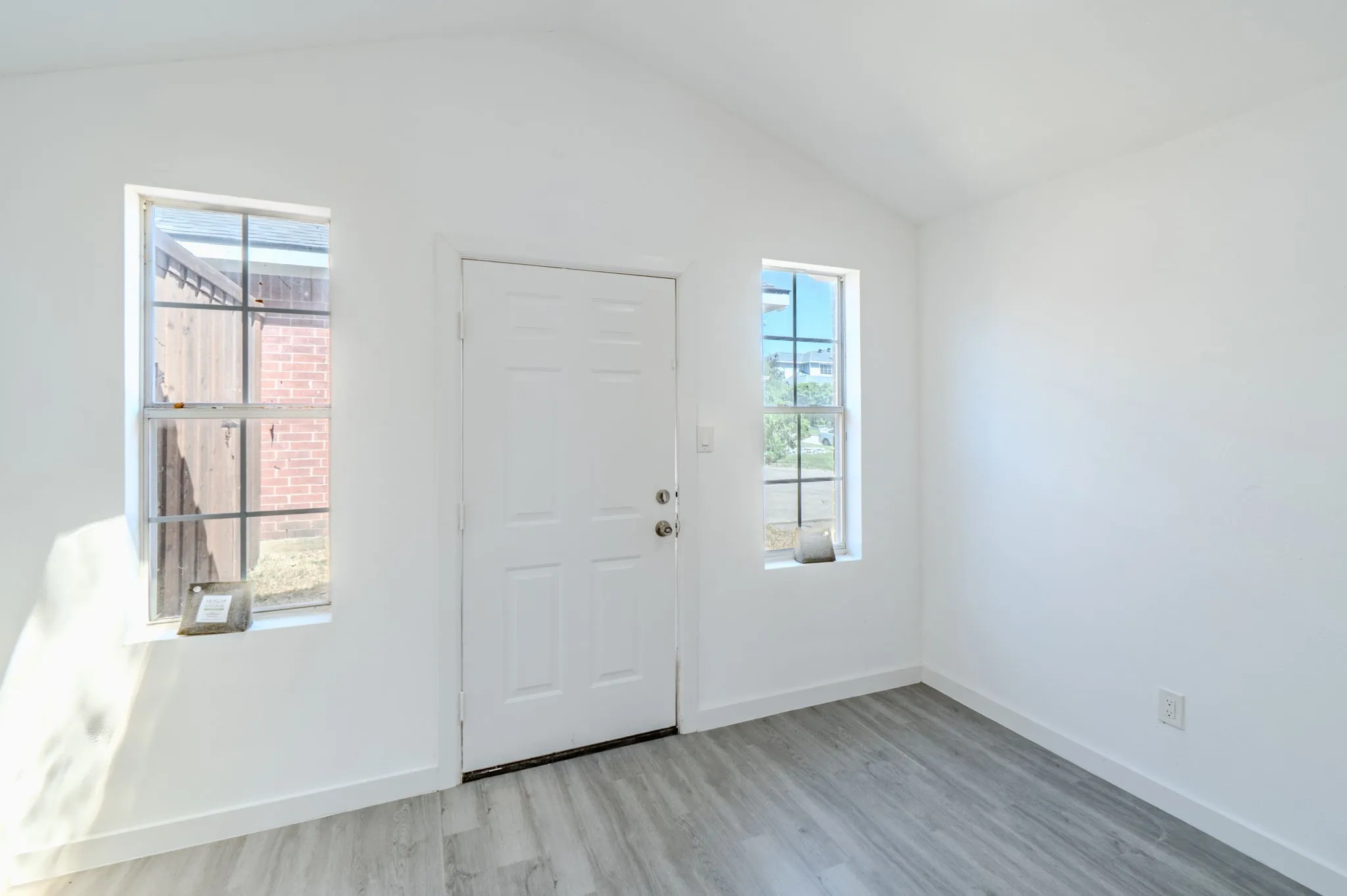 Interior space featuring a vaulted ceiling, wood-finish flooring, white walls, and a paneled entry door flanked by two windows