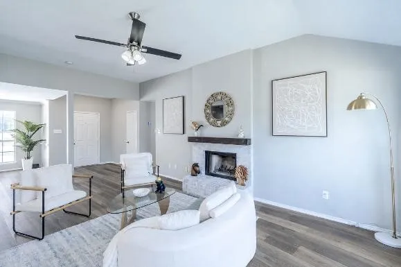 Vaulted ceiling, ceiling fan with integrated lighting, wood-finish flooring, fireplace with stone surround, and wood mantel