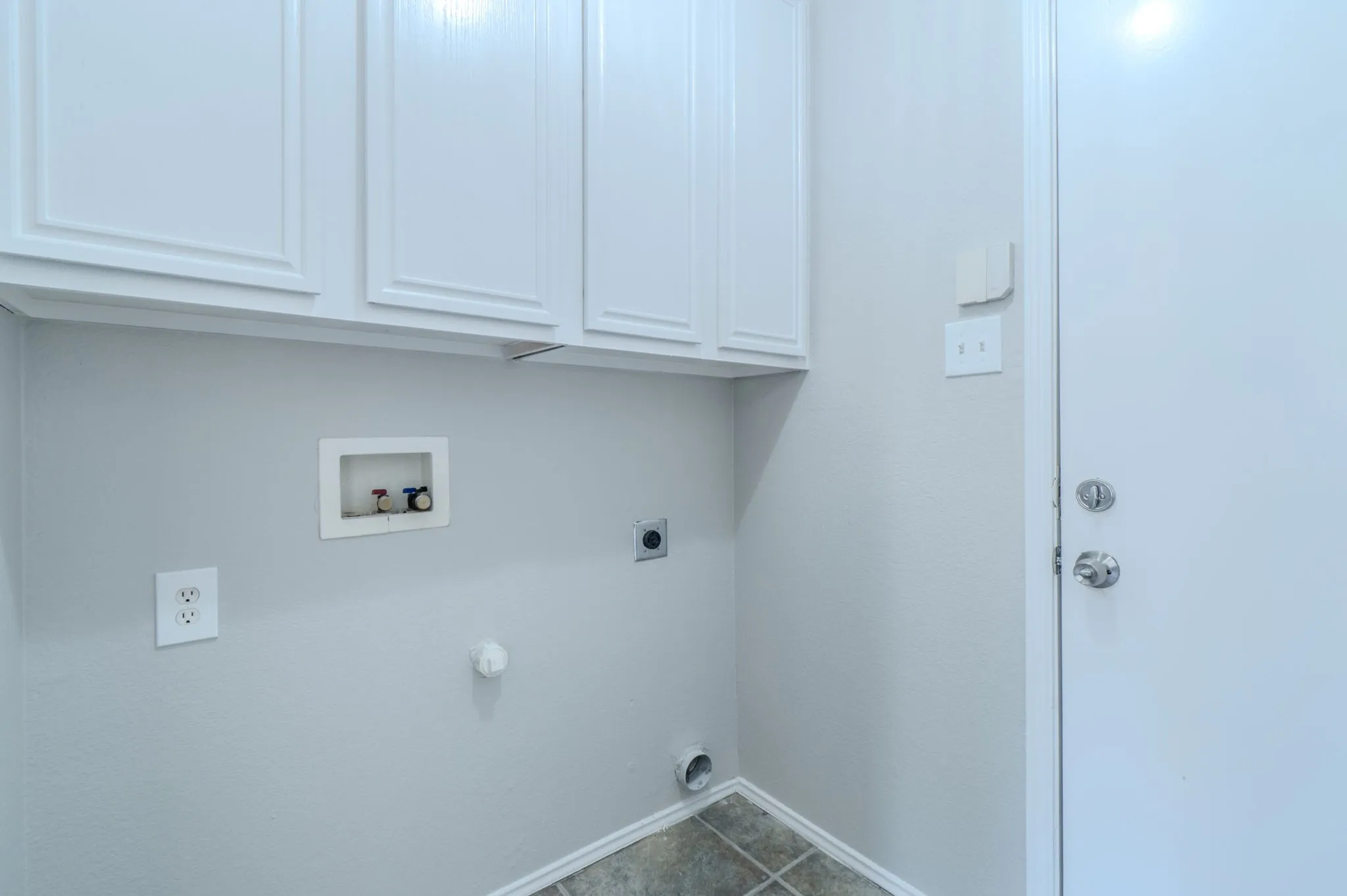 Utility area featuring white upper cabinetry, light gray wall paint, and a tiled floor