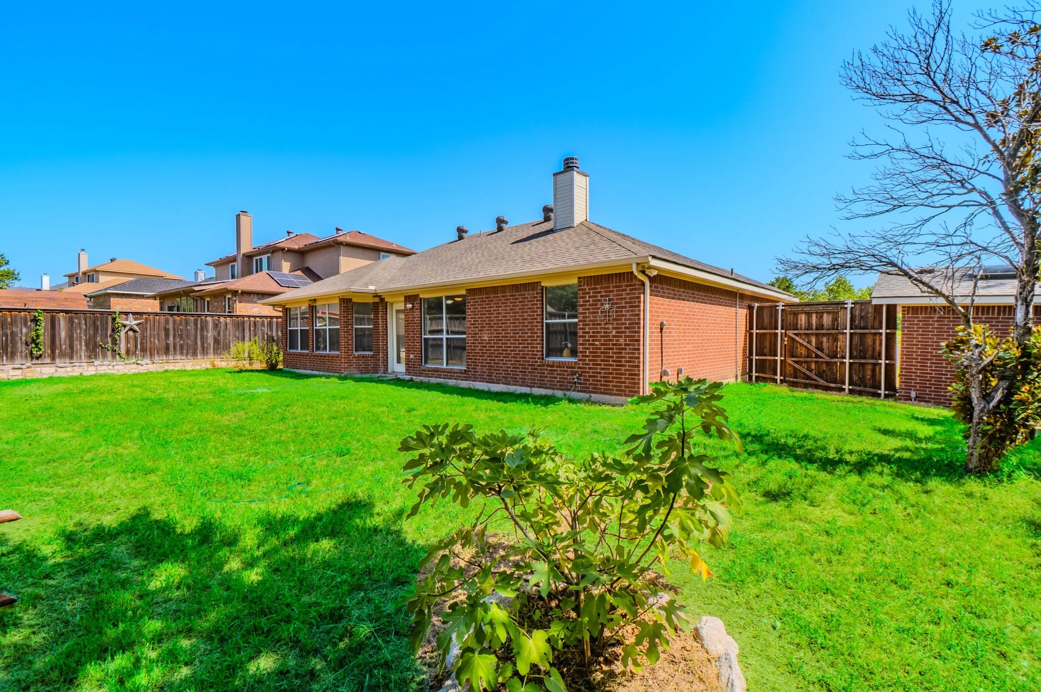 Generous backyard featuring a lush lawn, a brick exterior, multiple windows, a wood fence, and a gate
