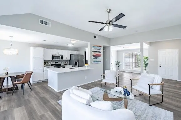 Vaulted ceiling living area featuring wood-finish flooring, a contemporary ceiling fan, and an open concept kitchen with white cabinetry and an island