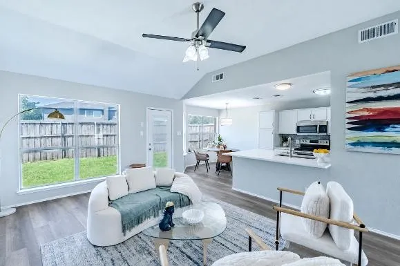 Vaulted ceiling with a ceiling fan, wood-finish flooring, recessed lighting, and a kitchen island with a sink