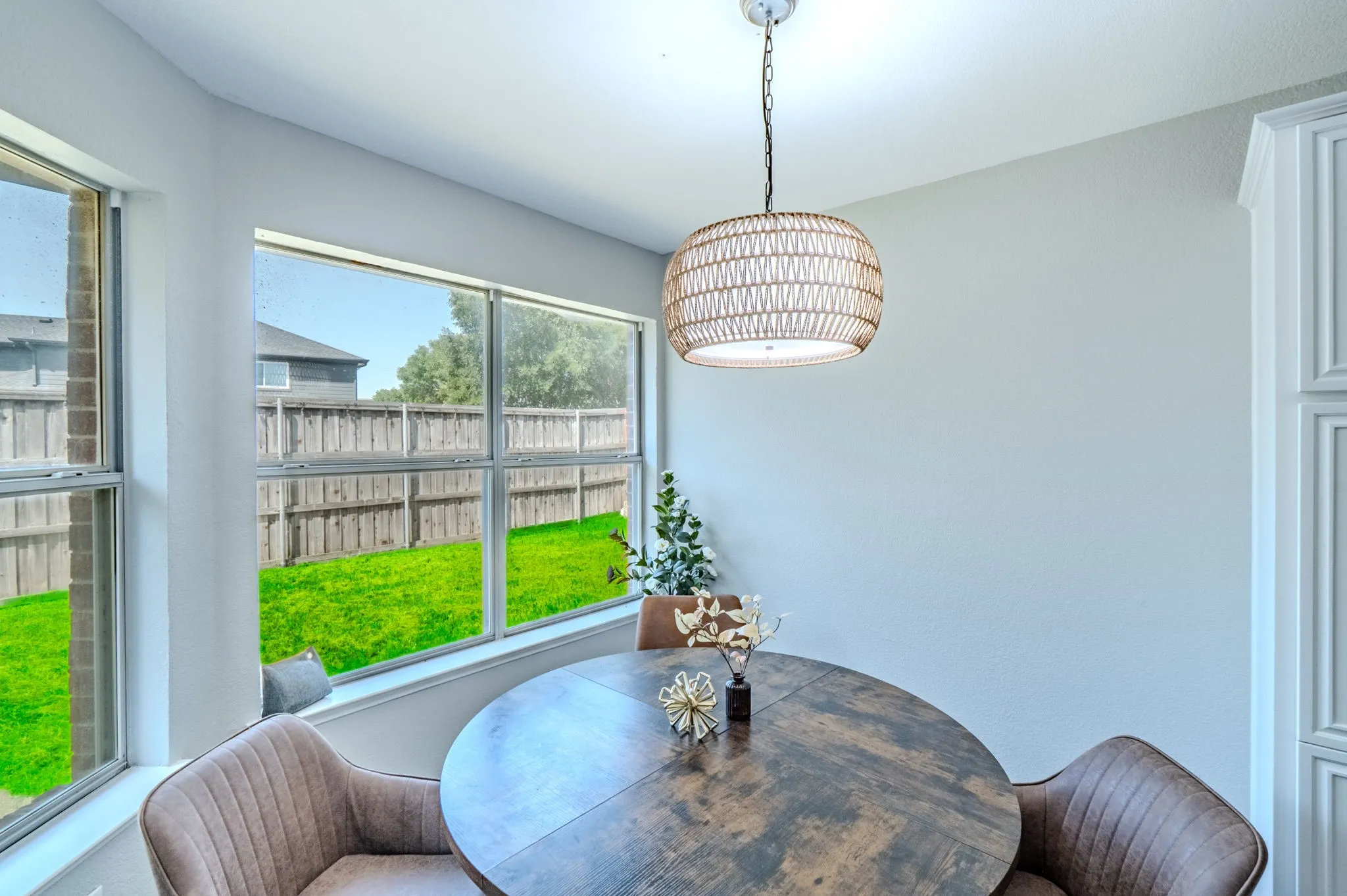 Bay window with multiple panes overlooking a fenced yard, overhead pendant lighting fixture, and paneled cabinetry
