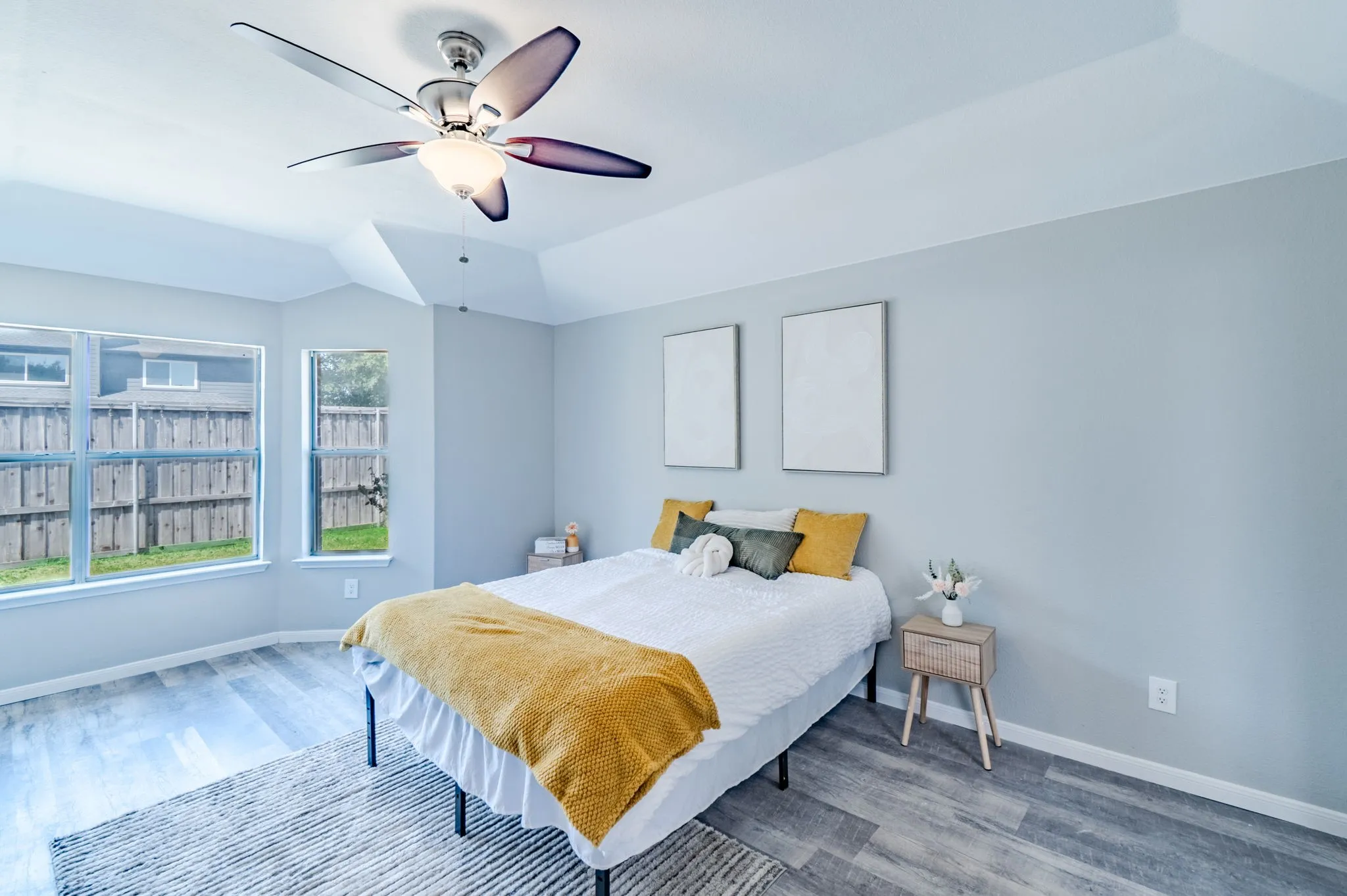 Bright bedroom featuring a tray ceiling, a modern ceiling fan with integrated lighting, wood-finish flooring, and multiple windows