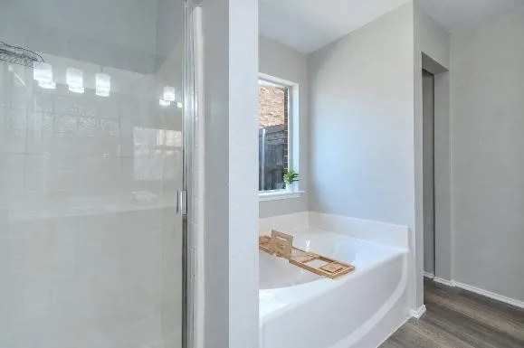 Glass-enclosed shower with white tiled walls, separate soaking tub, and wood-finish flooring
