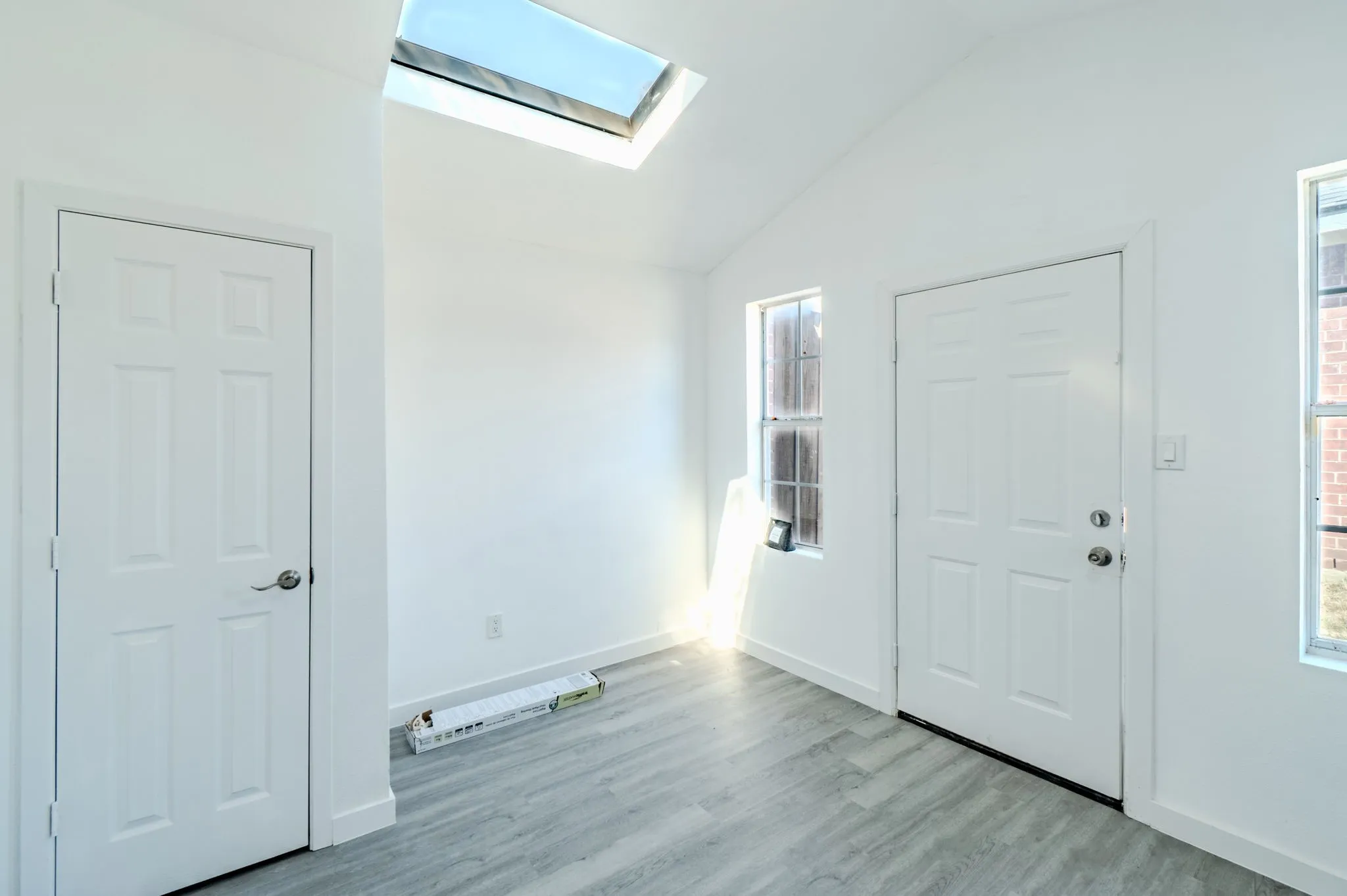 Vaulted ceiling with a skylight, white walls, and wood-finish flooring