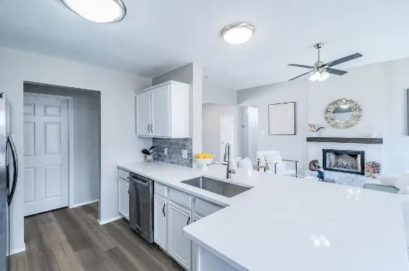 Kitchen featuring white cabinetry, light-toned countertops, a stainless steel dishwasher, and a tile backsplash