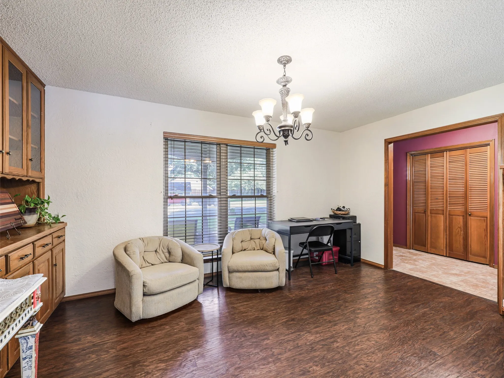 Living area featuring wood-finish flooring, a multi-pane window with blinds, and a built-in wood hutch with glass-front upper cabinets