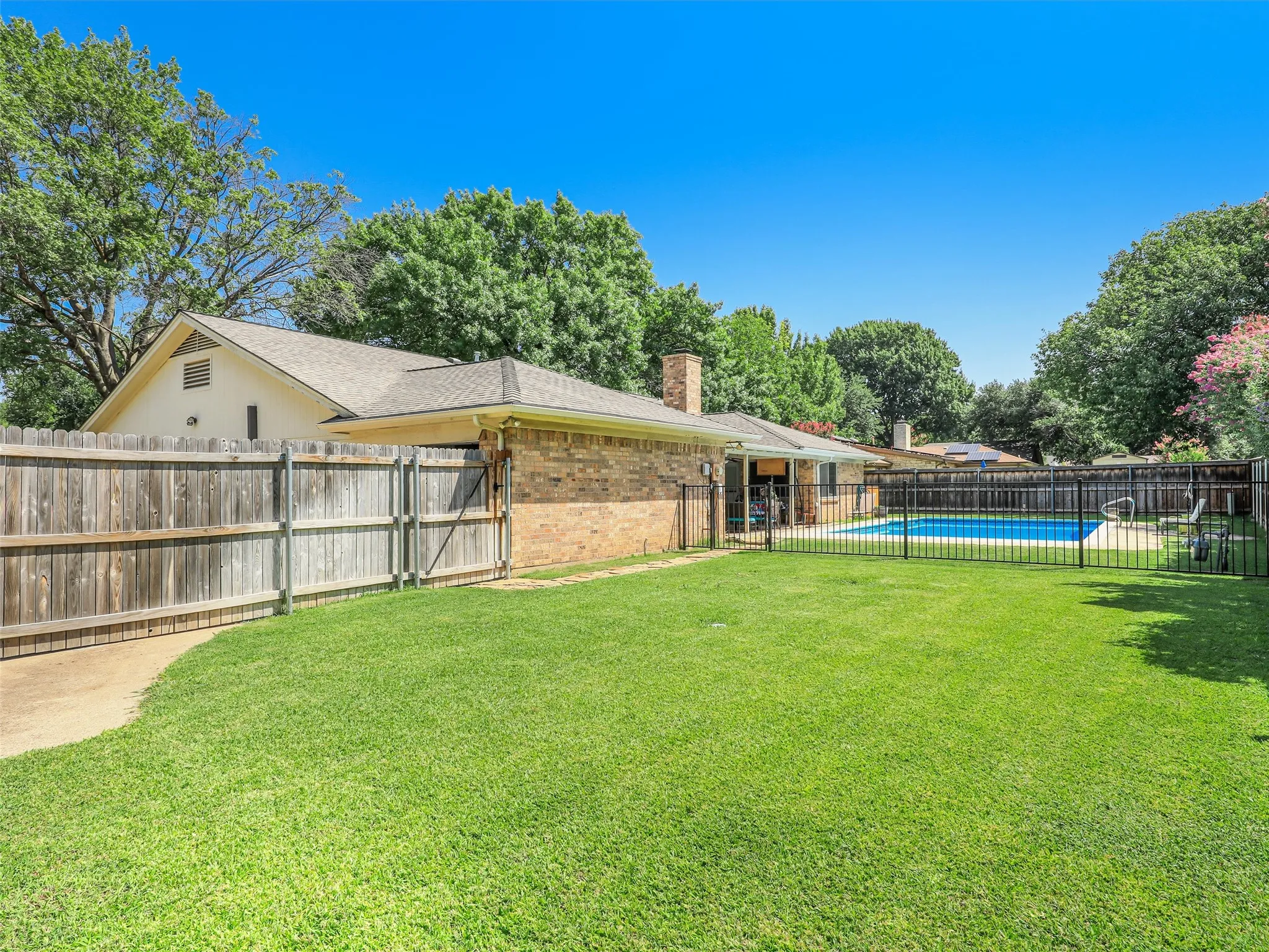 Expansive backyard featuring a lush lawn, privacy fencing, and a brick-clad residence