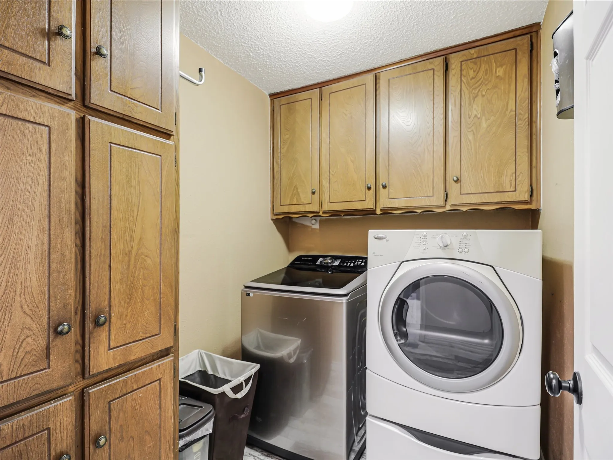 Dedicated laundry area featuring extensive wood-finish cabinetry, a front-loading washer, and a top-loading appliance