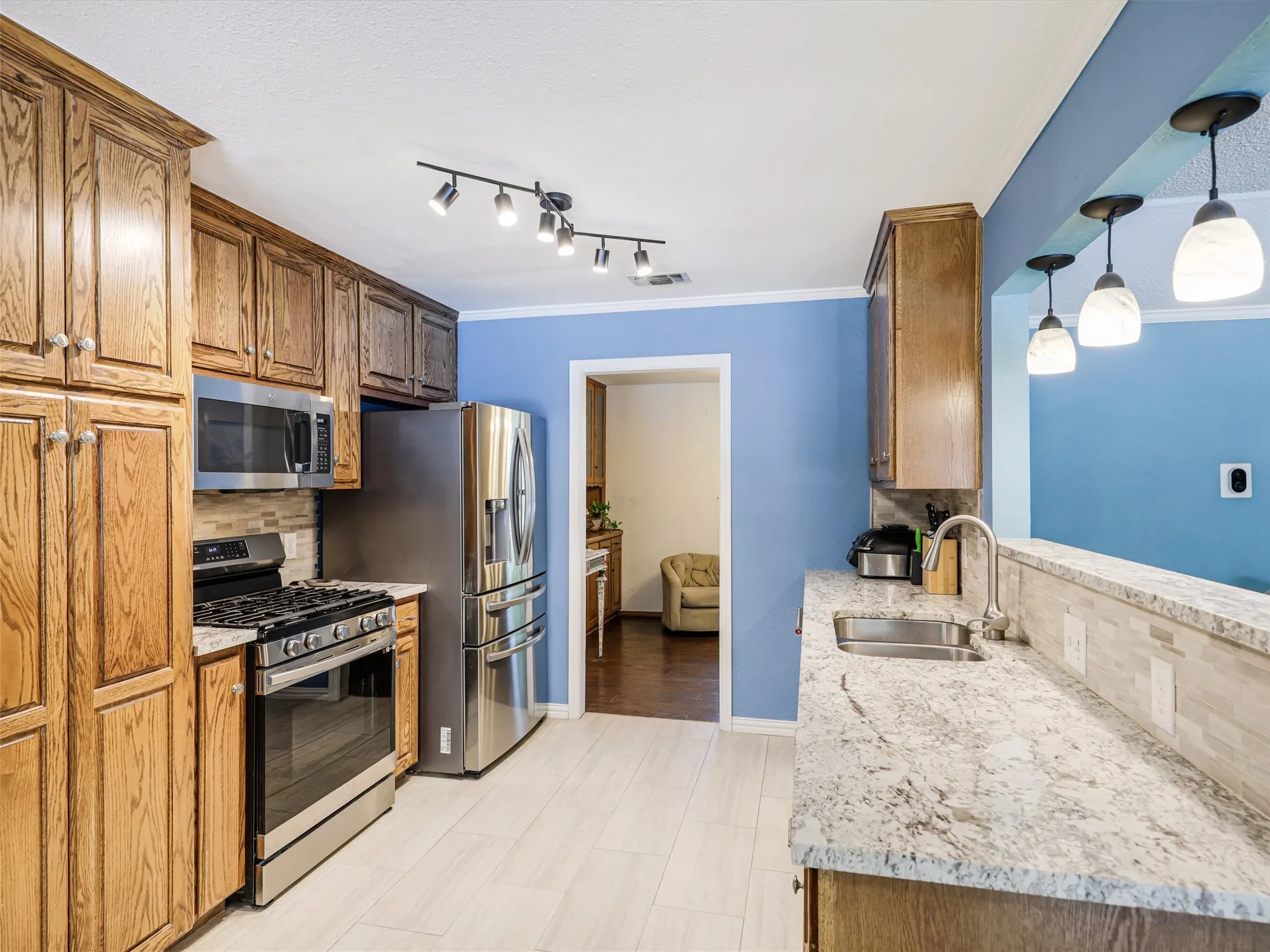 Kitchen featuring light wood-finish cabinetry, stainless steel appliances, speckled countertops with a tile backsplash, and light wood-finish flooring
