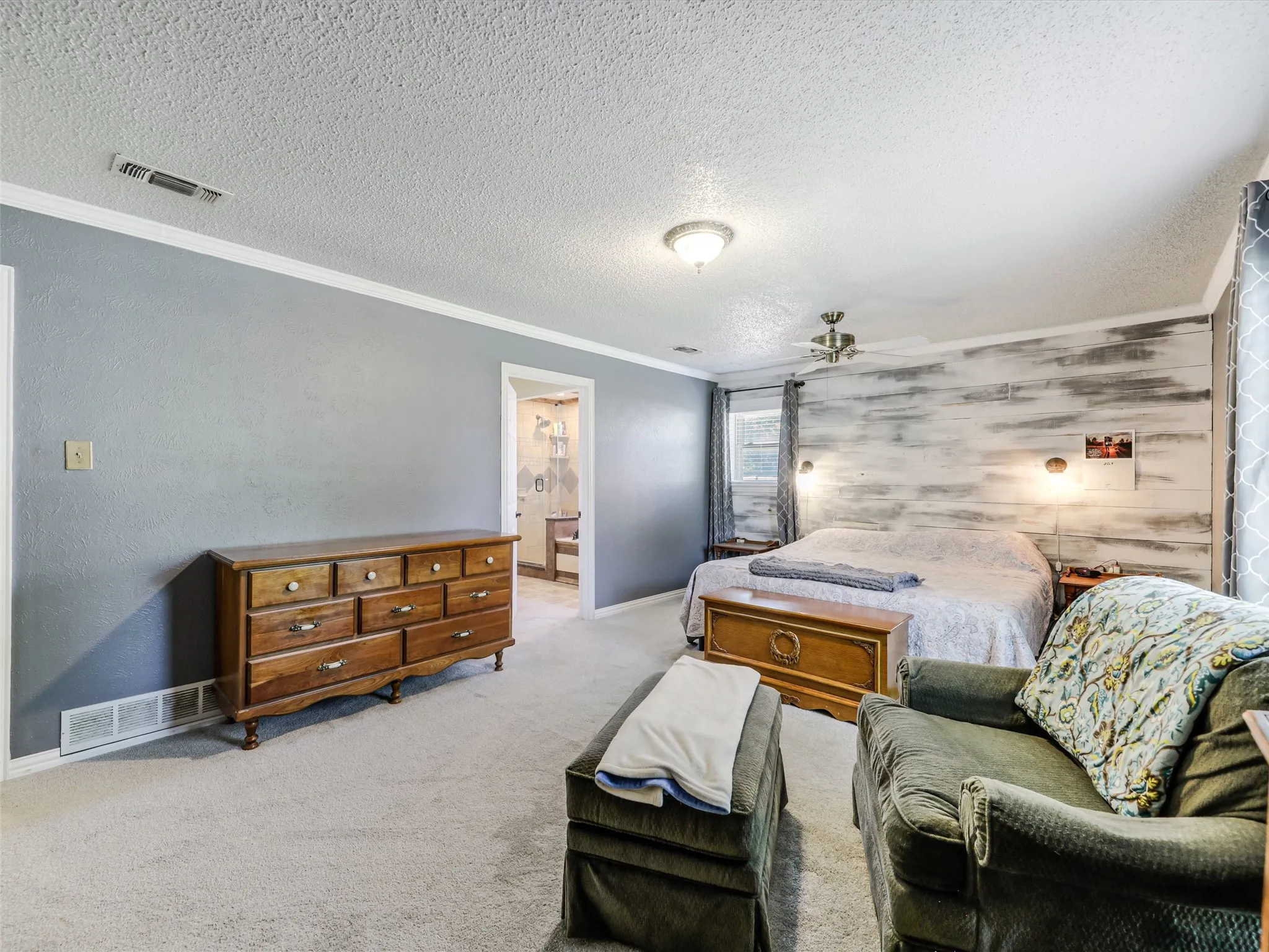 Carpeted bedroom featuring a textured accent wall, ceiling fan with integrated lighting, and a doorway revealing a bathroom with tiled walls